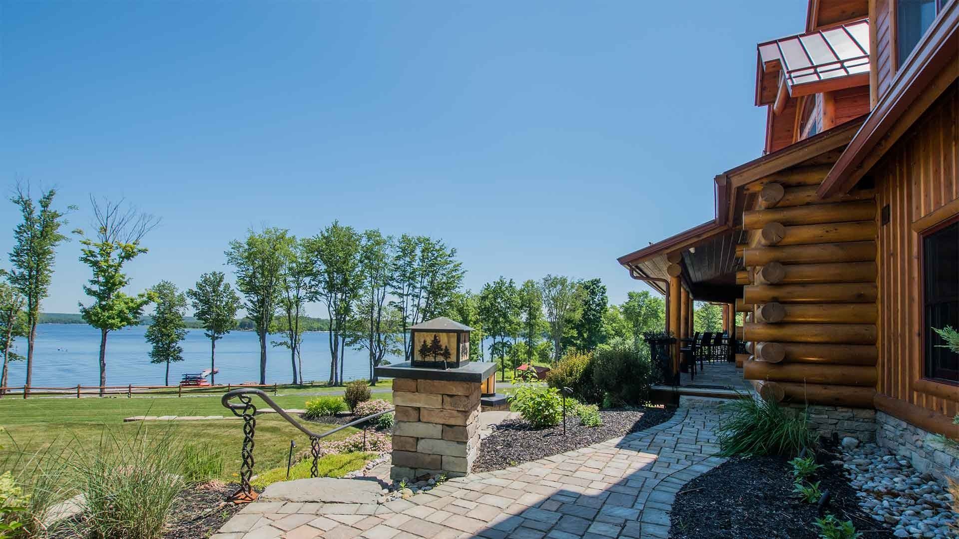 A log cabin with a walkway leading to it and a lake in the background.