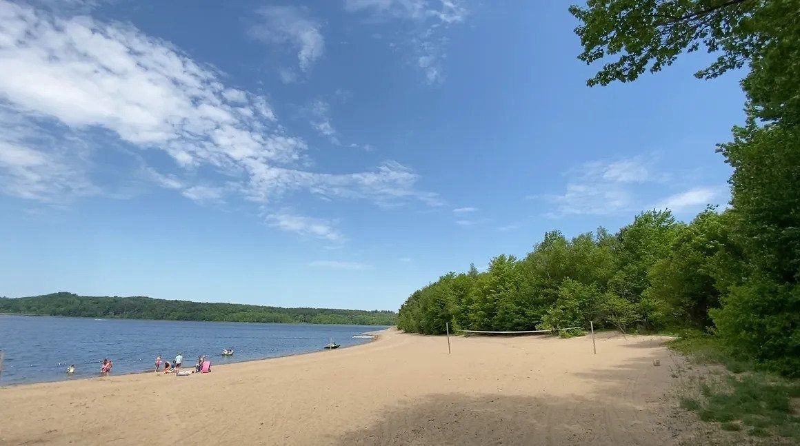 A sandy beach surrounded by trees and a lake on a sunny day.