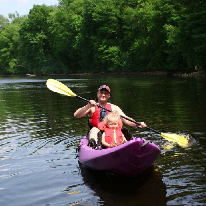 A man and child are paddling a purple kayak on a river
