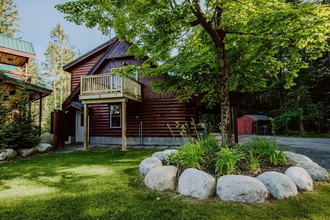 A log cabin with a balcony and a lot of rocks in front of it.
