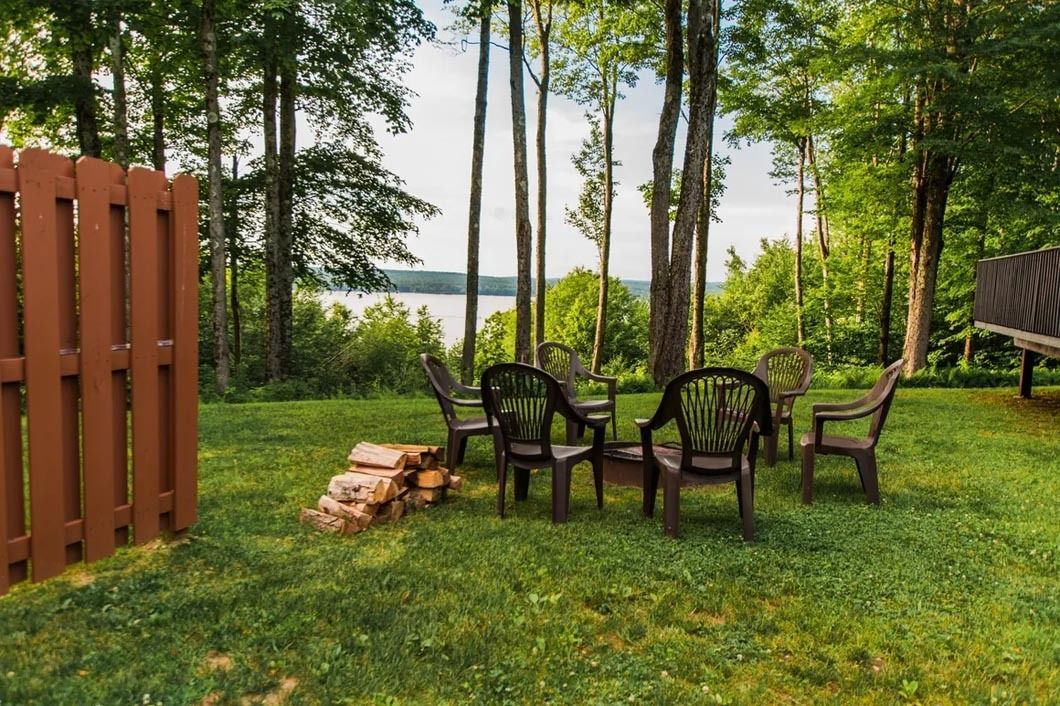 A lawn with chairs , tables and a fire pit in the middle of it.