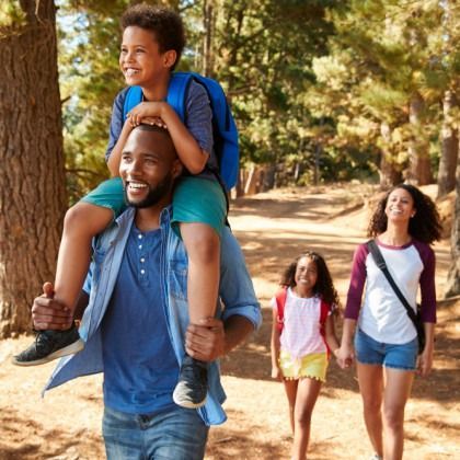 A man is carrying a child on his shoulders while a woman and two children walk behind him.