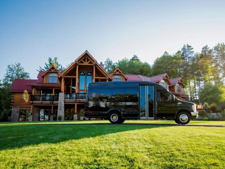A black van is parked in front of a large log cabin.