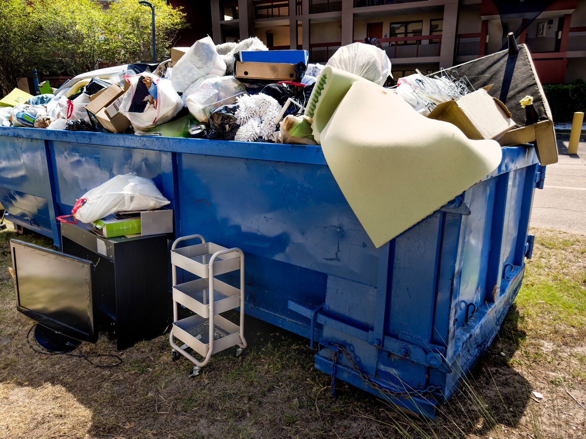 A blue dumpster filled with lots of trash and junk.