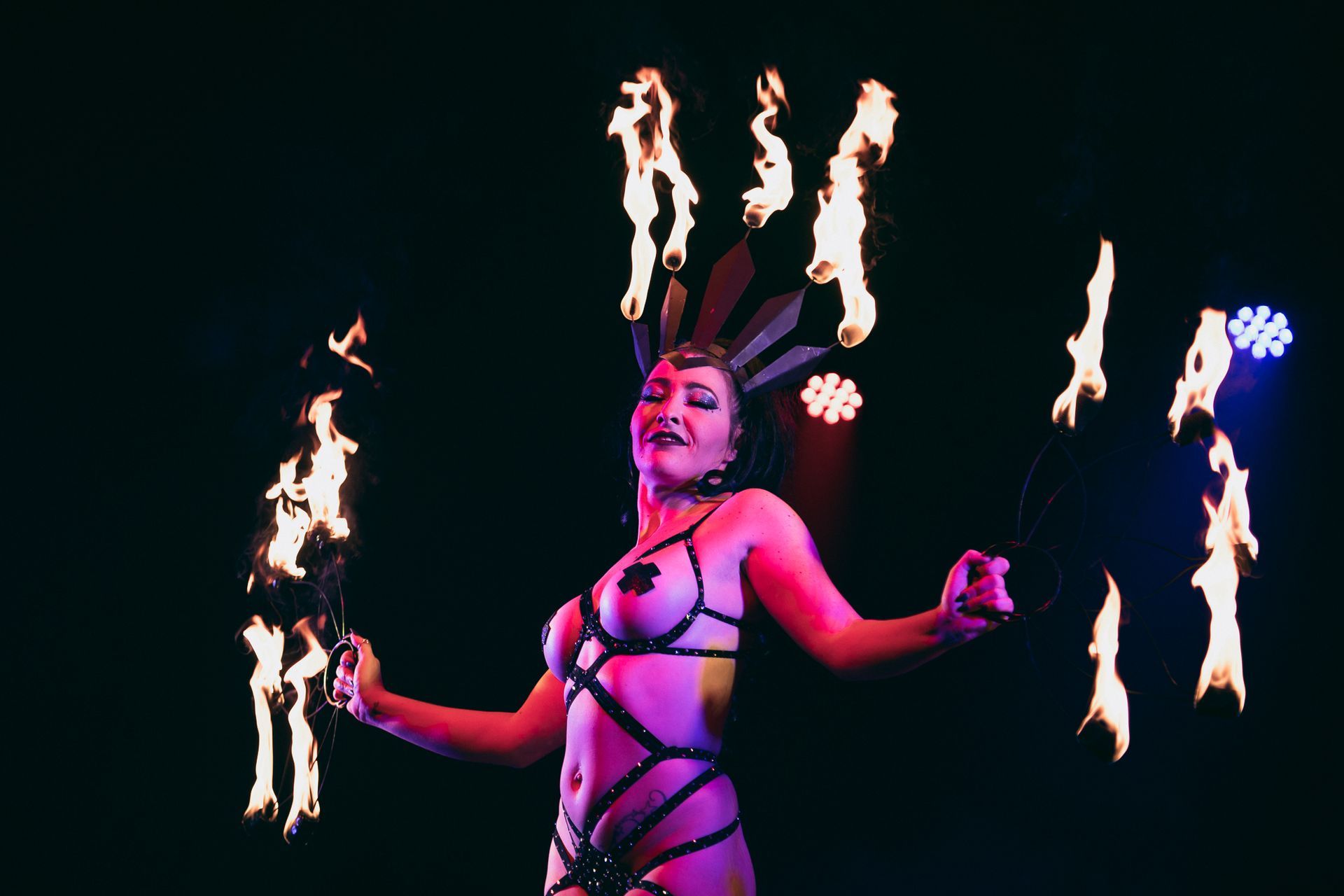 Woman in lingerie performs fire dance with torches, stage lit, dark background.