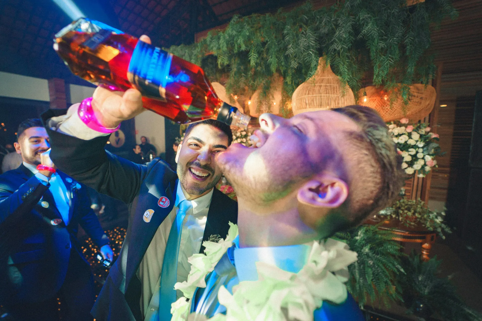 Man wearing floral necklace drinking rum at bachelor party.