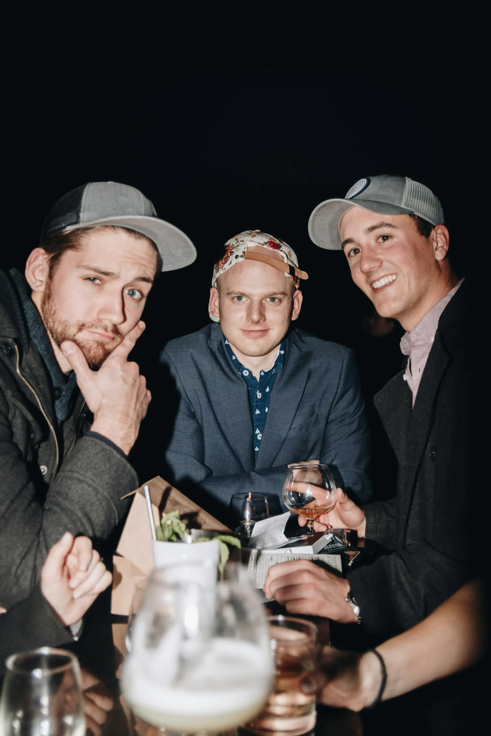 Three young men sitting together, smiling at the camera, enjoying alcoholic drinks