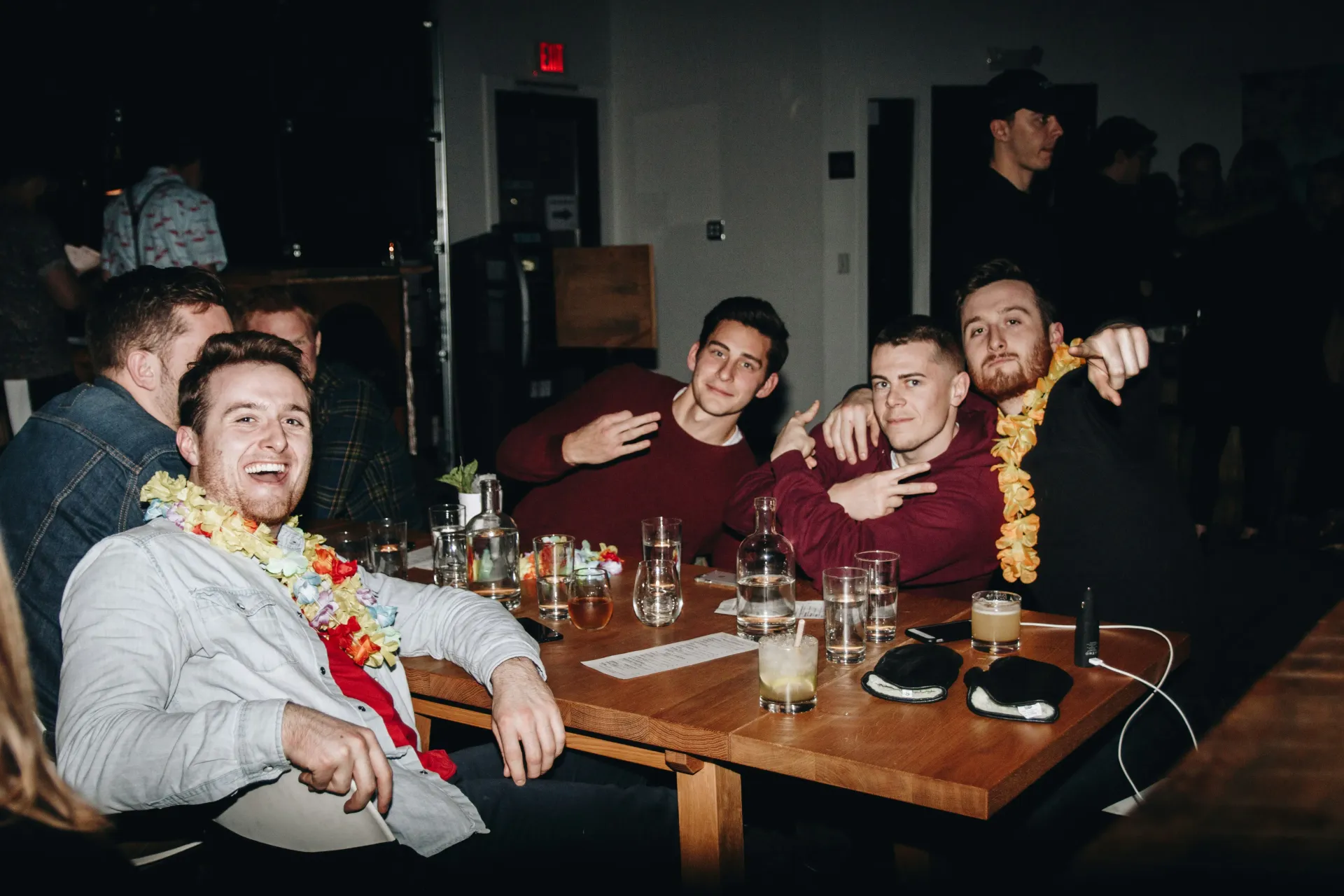 Group of young men celebrating a bachelor party at a table in dimly lit setting, smiling.