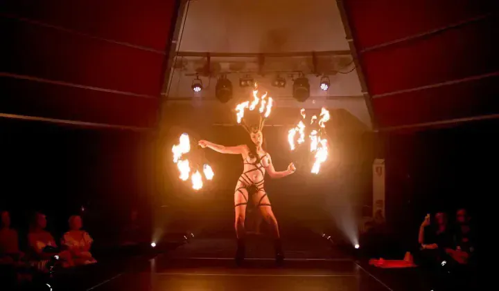 Fire dancer twirling flaming objects on stage, surrounded by dim lights and audience.