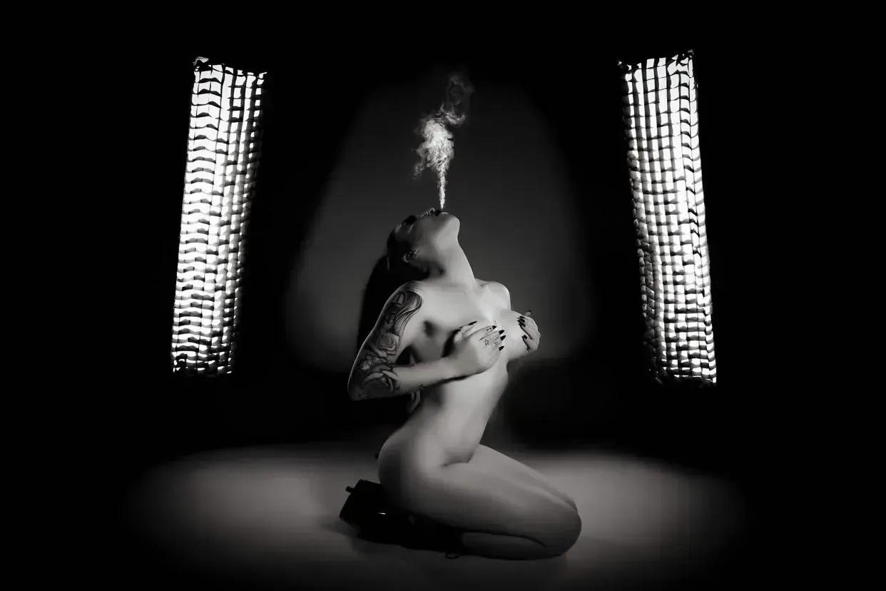 Nude fire dancer blowing smoke in the air, black and white photo.