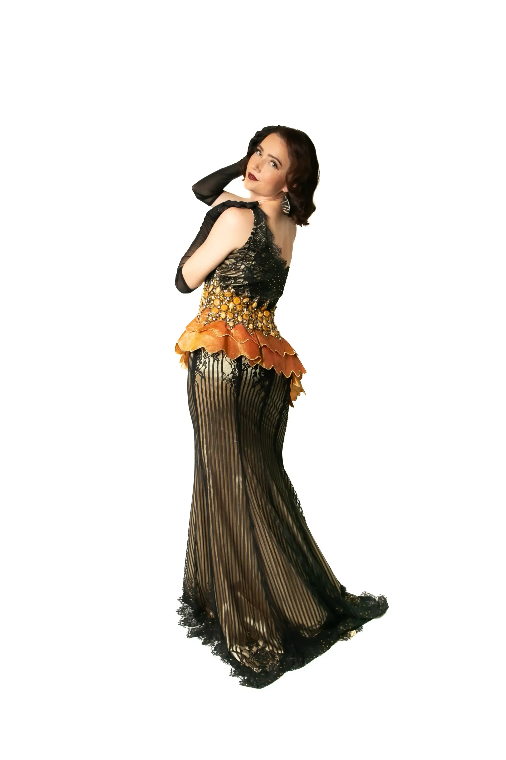 Burlesque performer in a black lace evening gown, posing with long black gloves, in studio.