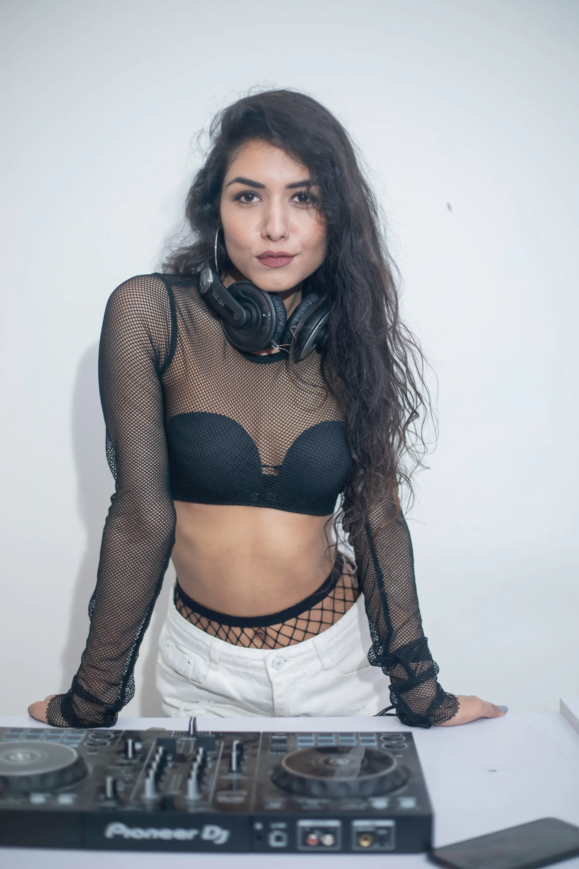 Brunett DJ, balck top, black headset around neck, fishnet stockings.