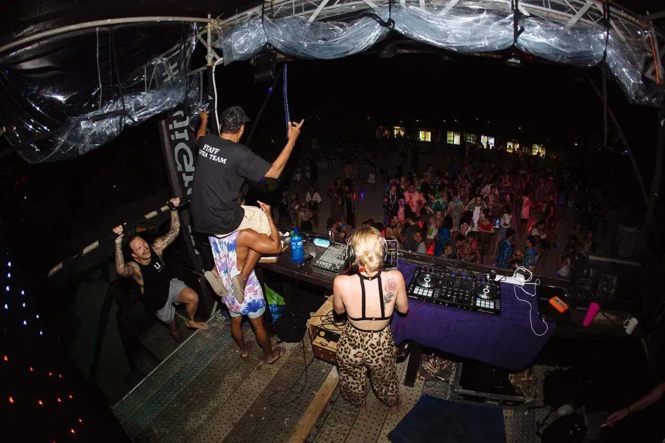 DJ and crowd at an outdoor music festival at night; people dancing and lights overhead.