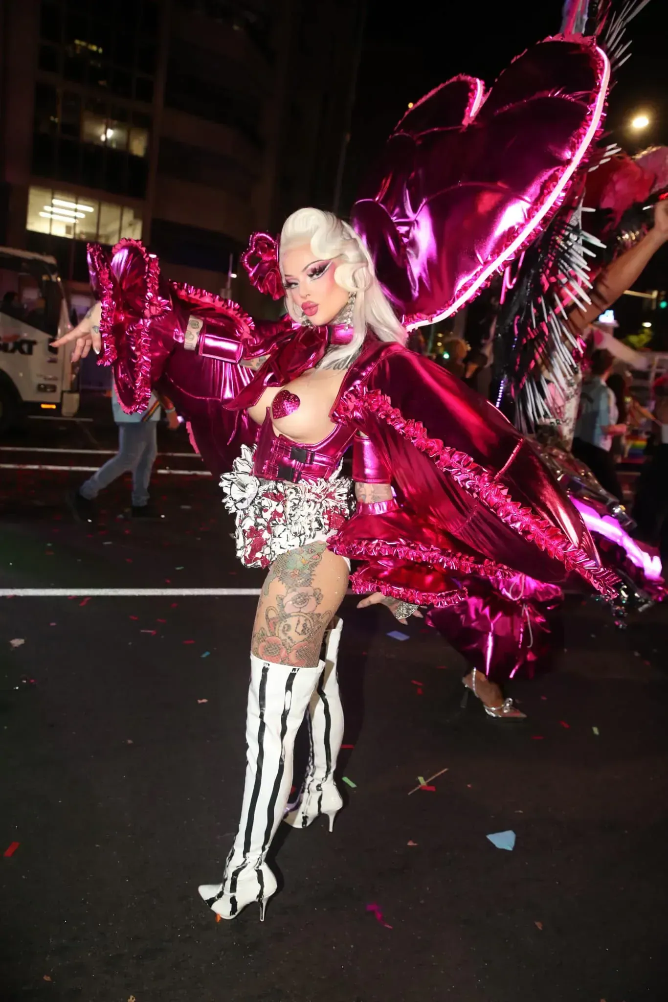 Drag performer in pink inflatable heart costume and striped boots at street event.