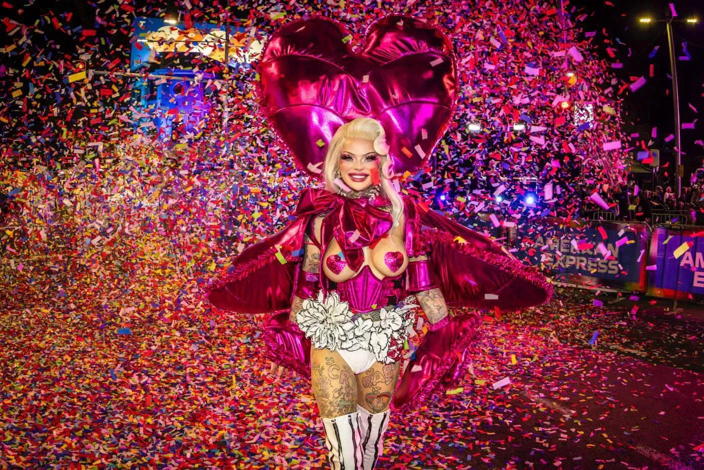 Drag performer in pink heart-shaped attire amid confetti.