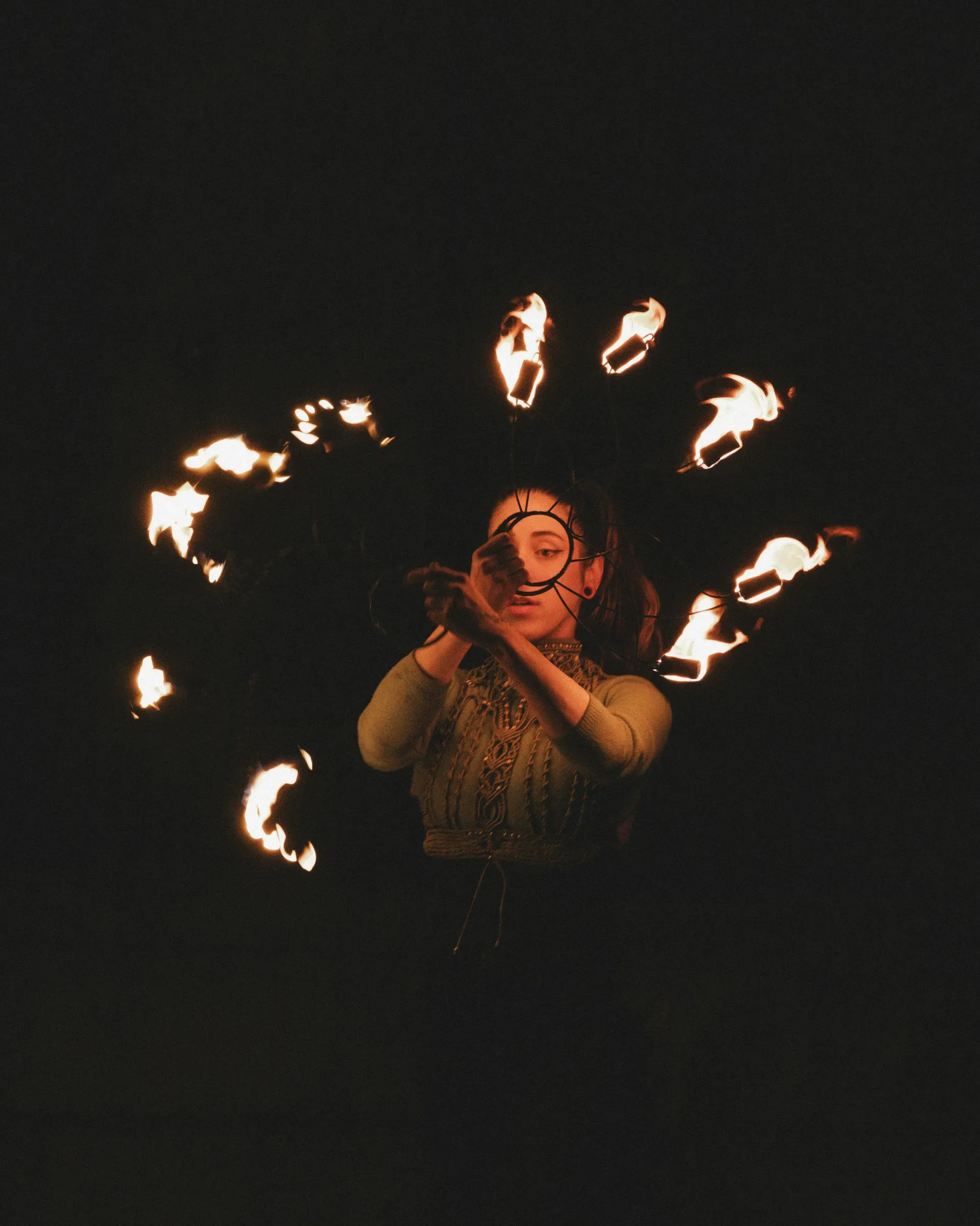 Fire dancer spinning a fire fan, creating a ring of flames against dark background.