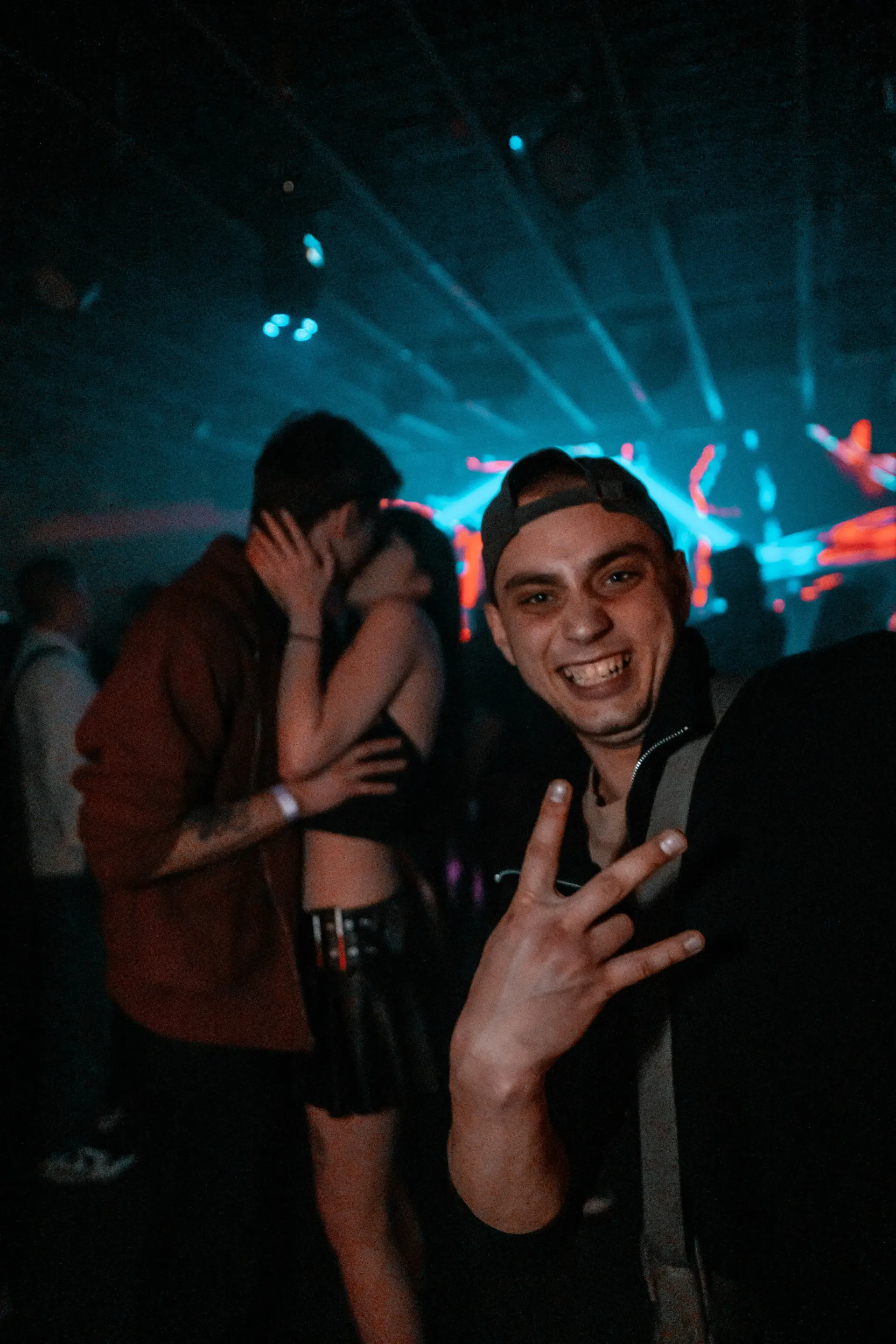 Man at a nightclub photo bombing a couple kissing.