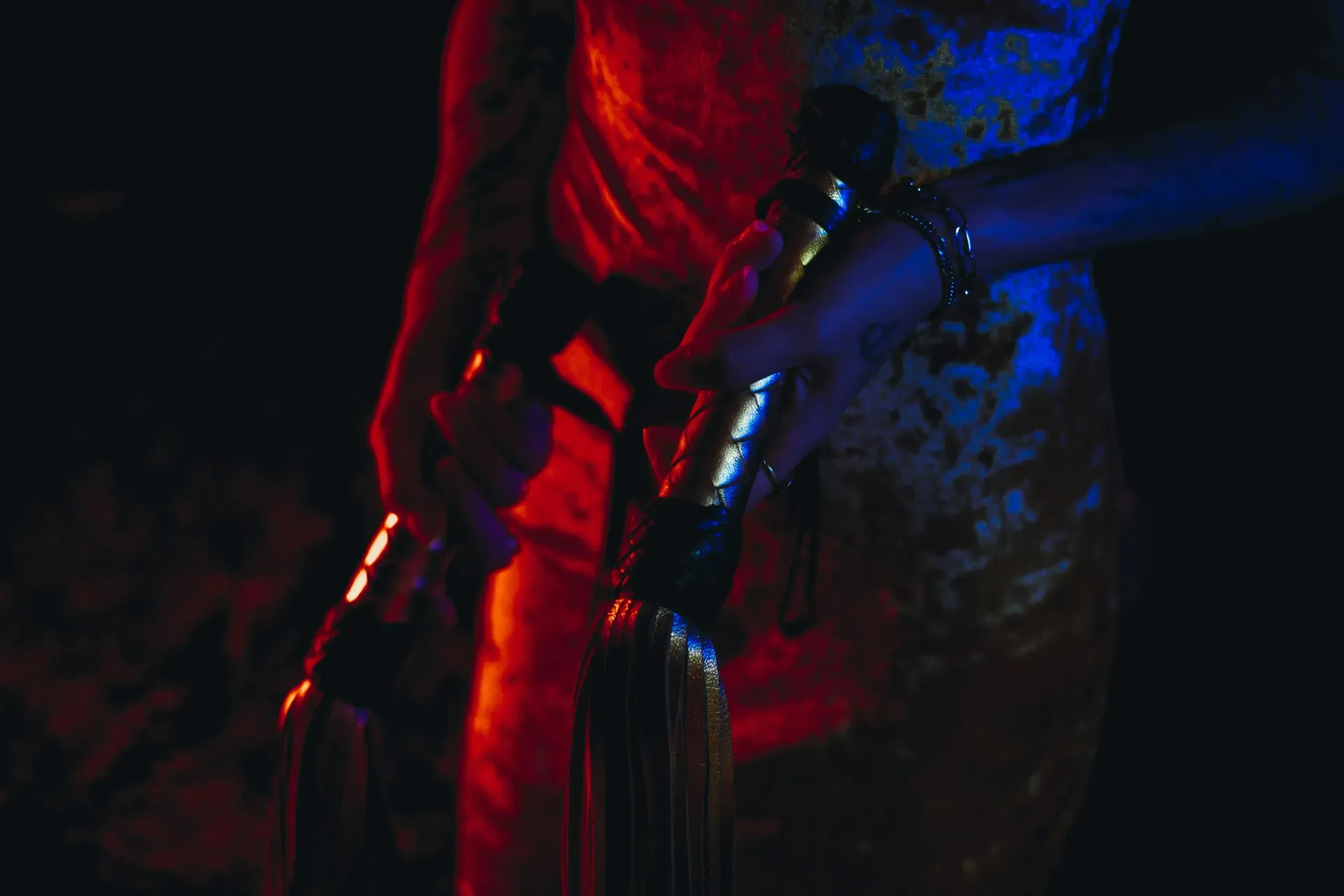 Stripper holding two whip tassels in red and blue lighting.