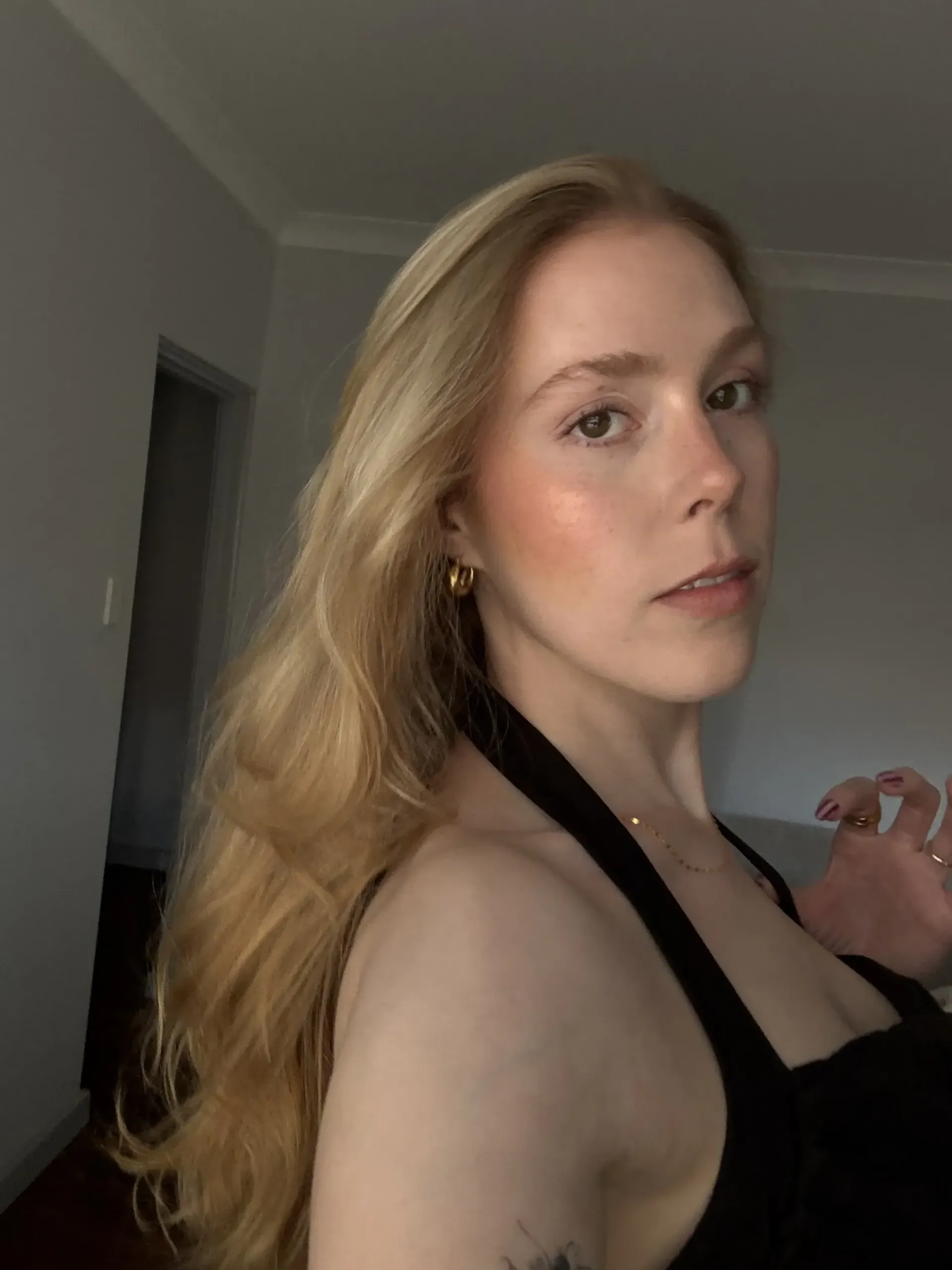 Woman with long blonde hair, wearing a black halter top, looking at camera.