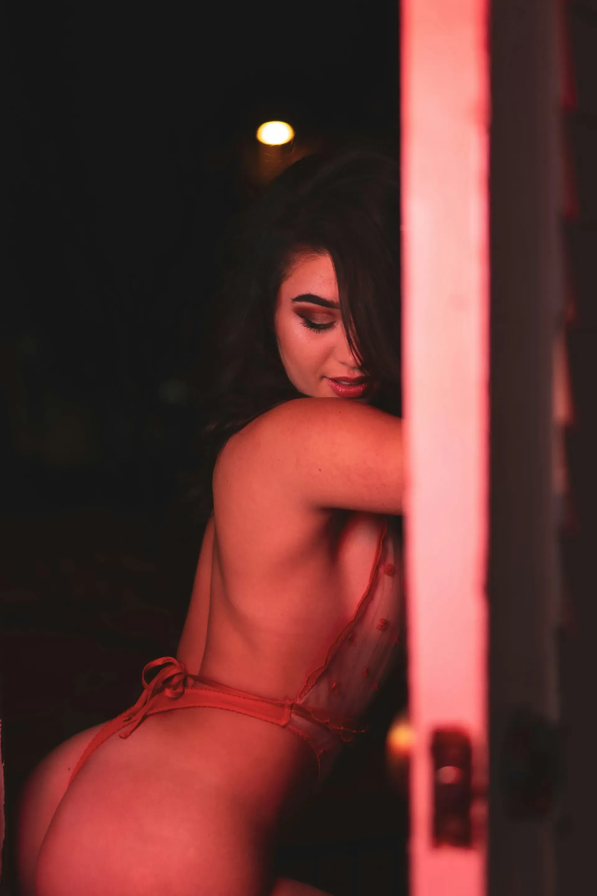 Lingerie model wearing red lingeiere posing against a door.