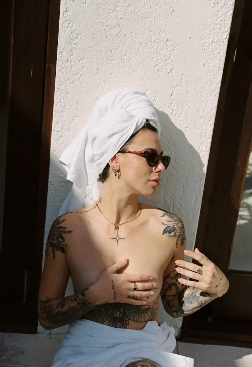 Topless waitress wearing sunglasses, towel on head and wrapped around waist, partially covers chest.