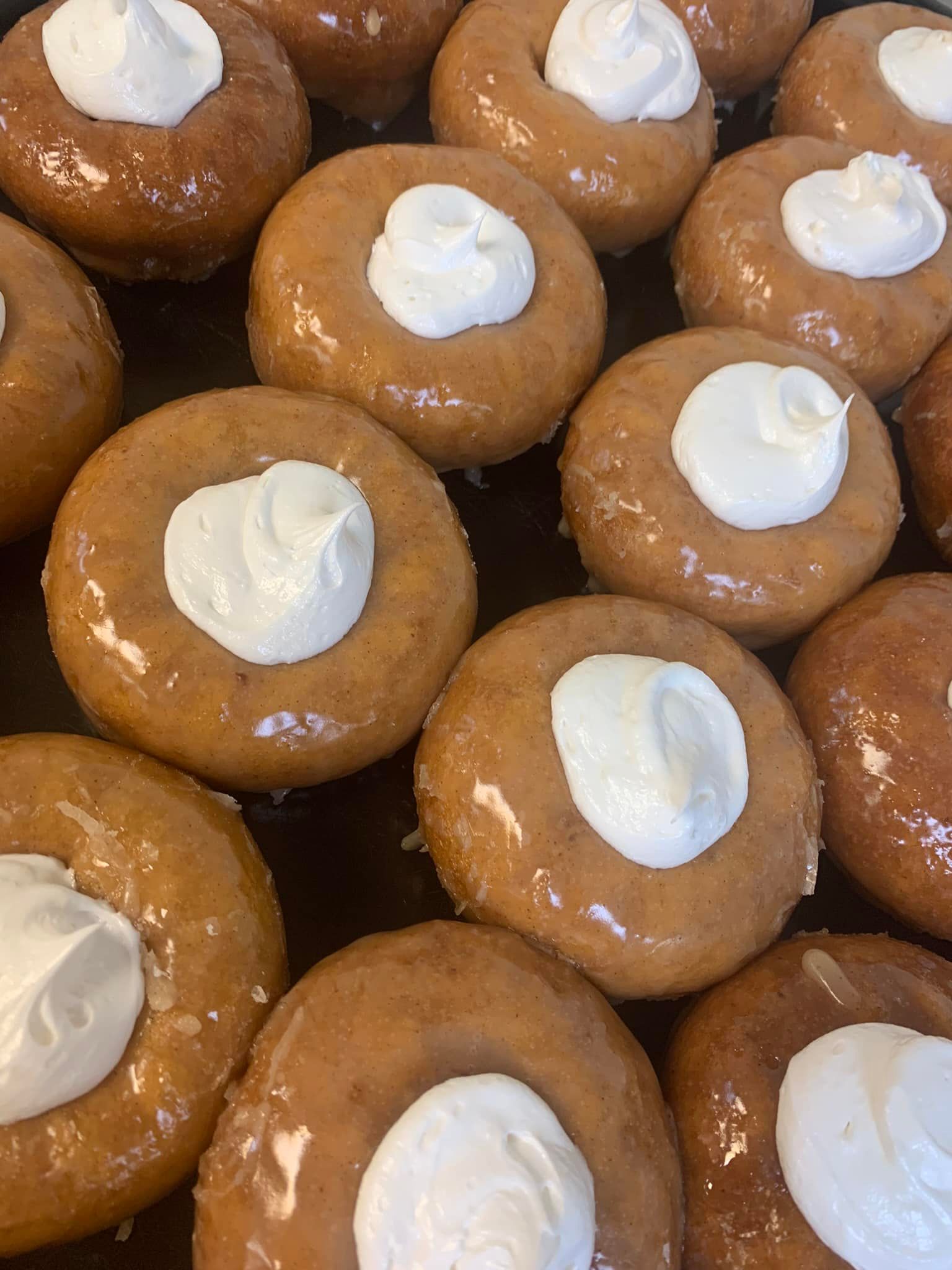 Close-up of glazed donuts with white icing drizzle and cream topping, arranged on a dark surface.