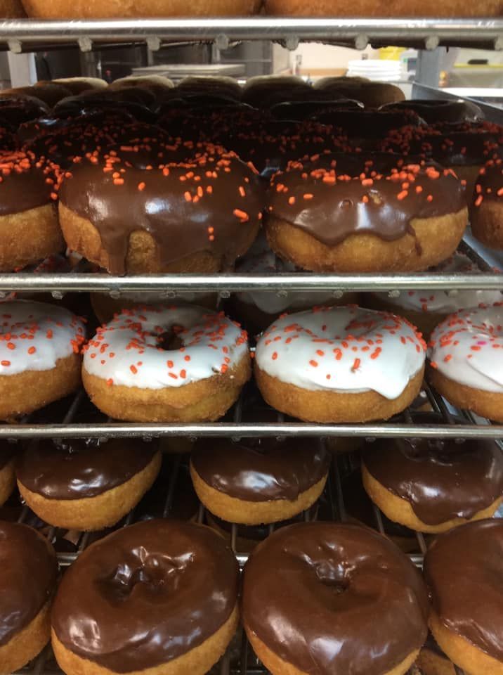 Donuts on tiered racks, with chocolate and white frosting and orange sprinkles.