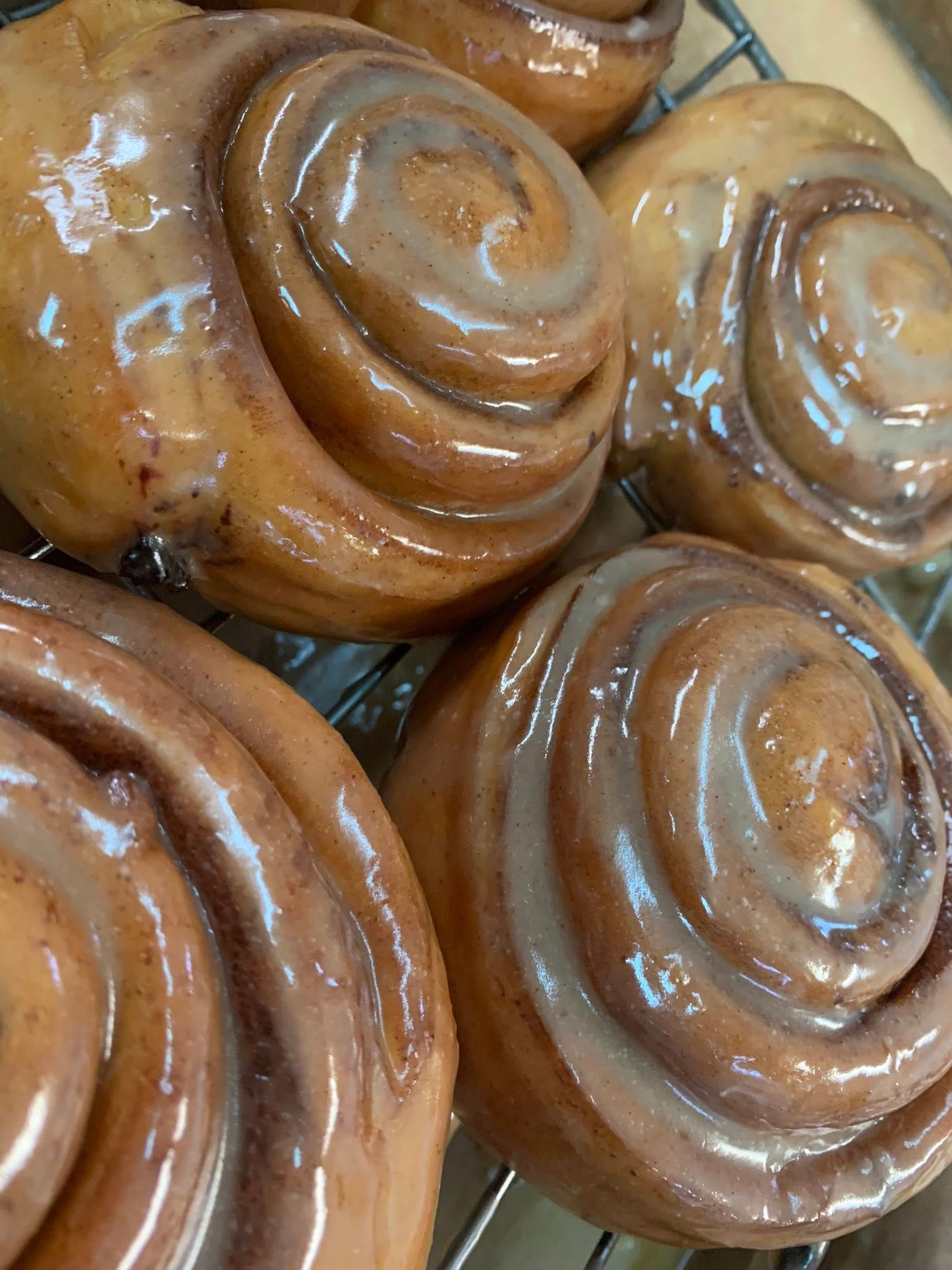 Cinnamon rolls with shiny glaze, on a cooling rack, close-up.