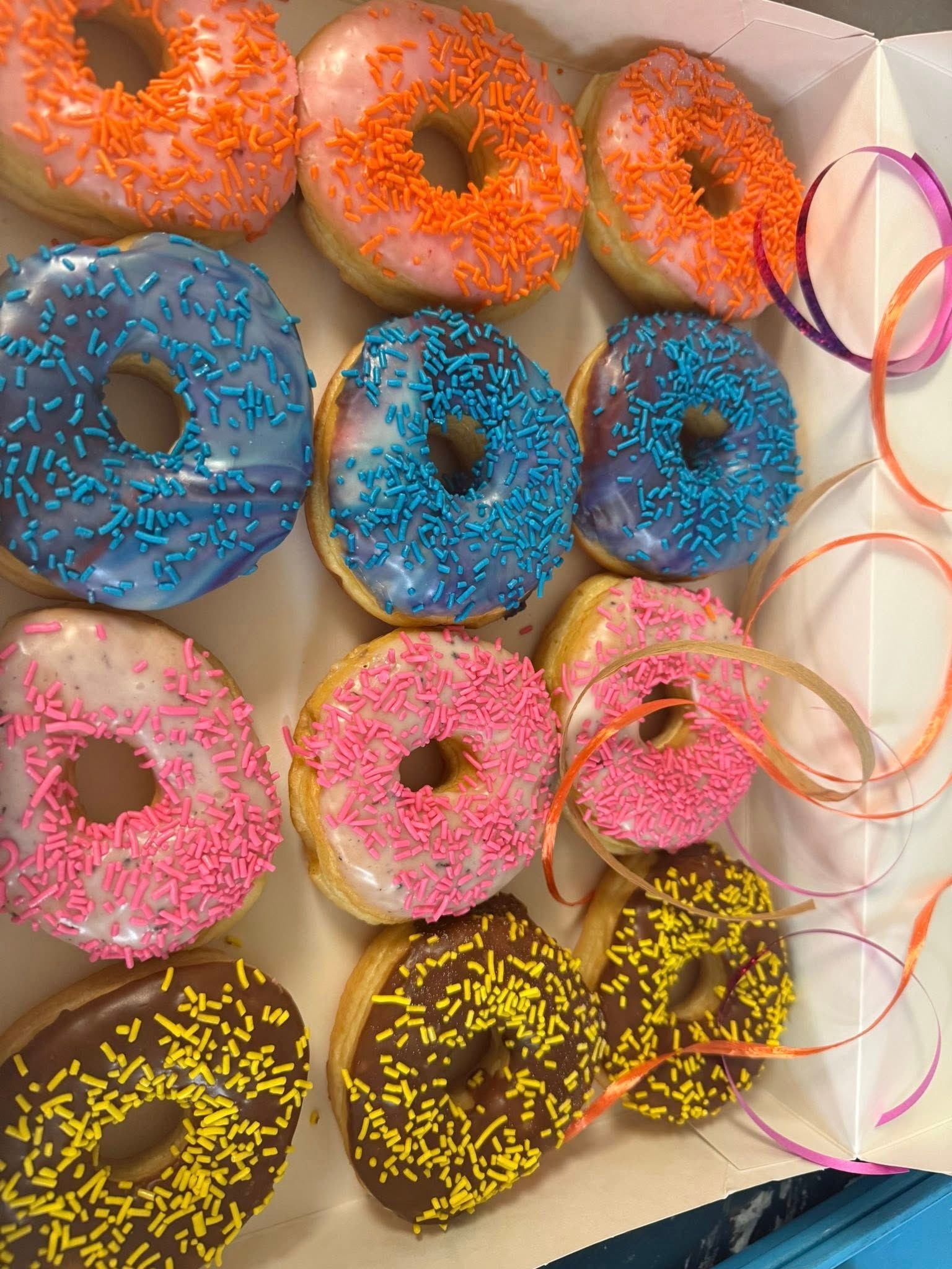 Box of a dozen frosted donuts with colorful sprinkles.