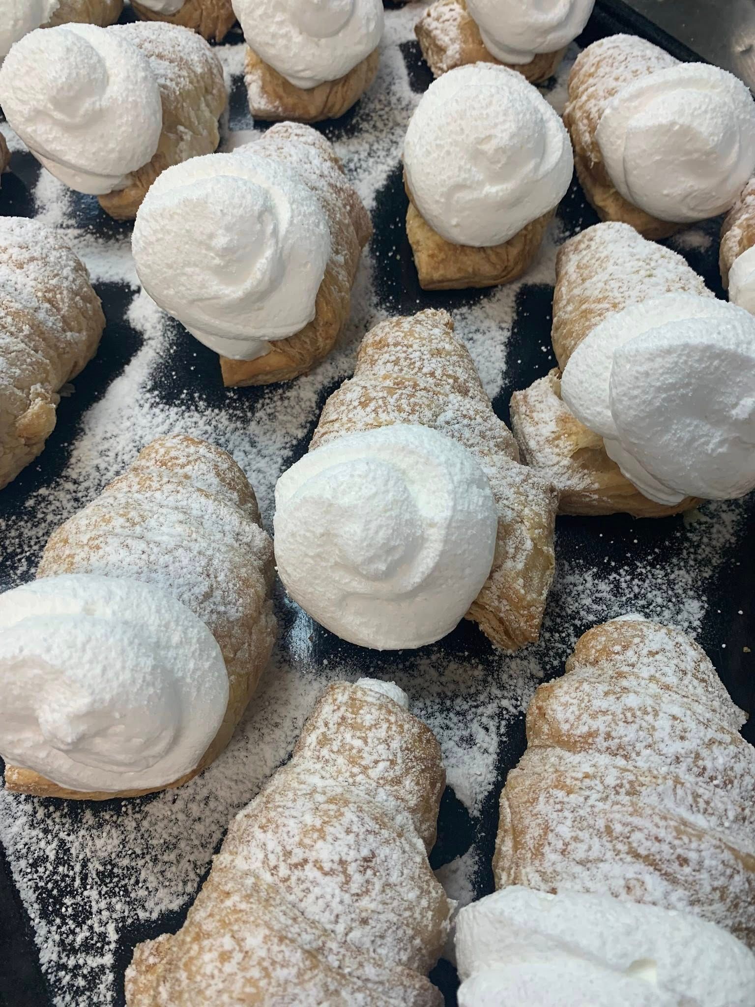 Pastries with whipped cream, dusted with powdered sugar, arranged on a tray.