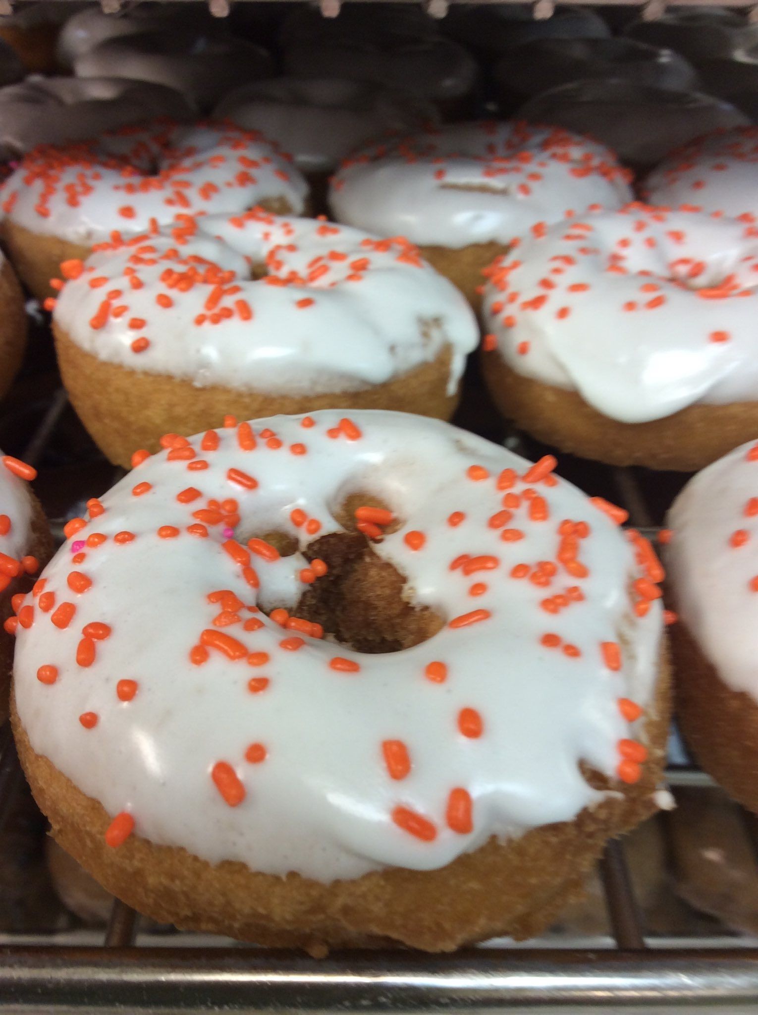 Donuts with white frosting and orange sprinkles displayed on a metal rack.