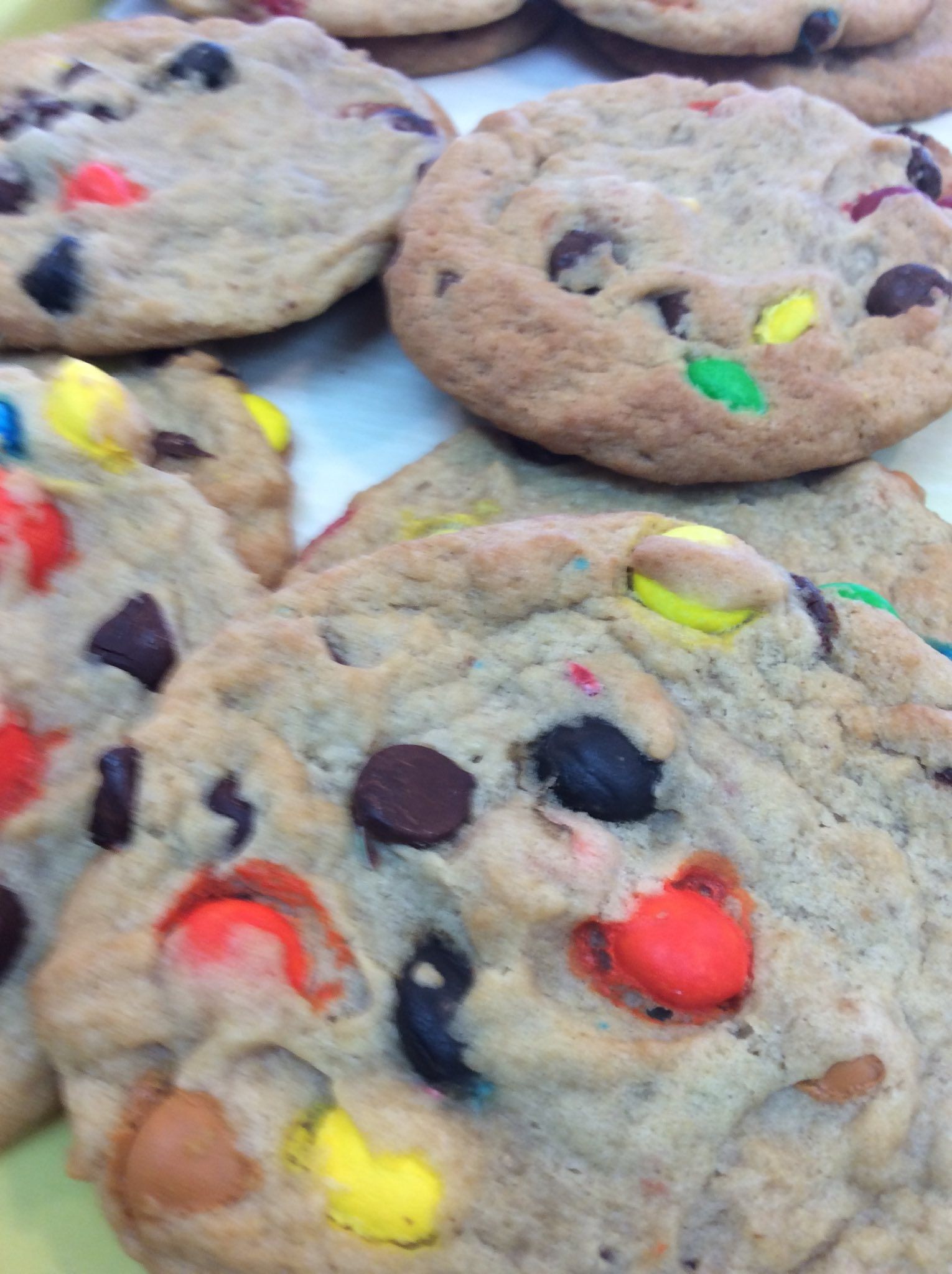 Close-up of several round cookies, speckled with colorful M&M candies and chocolate chips.