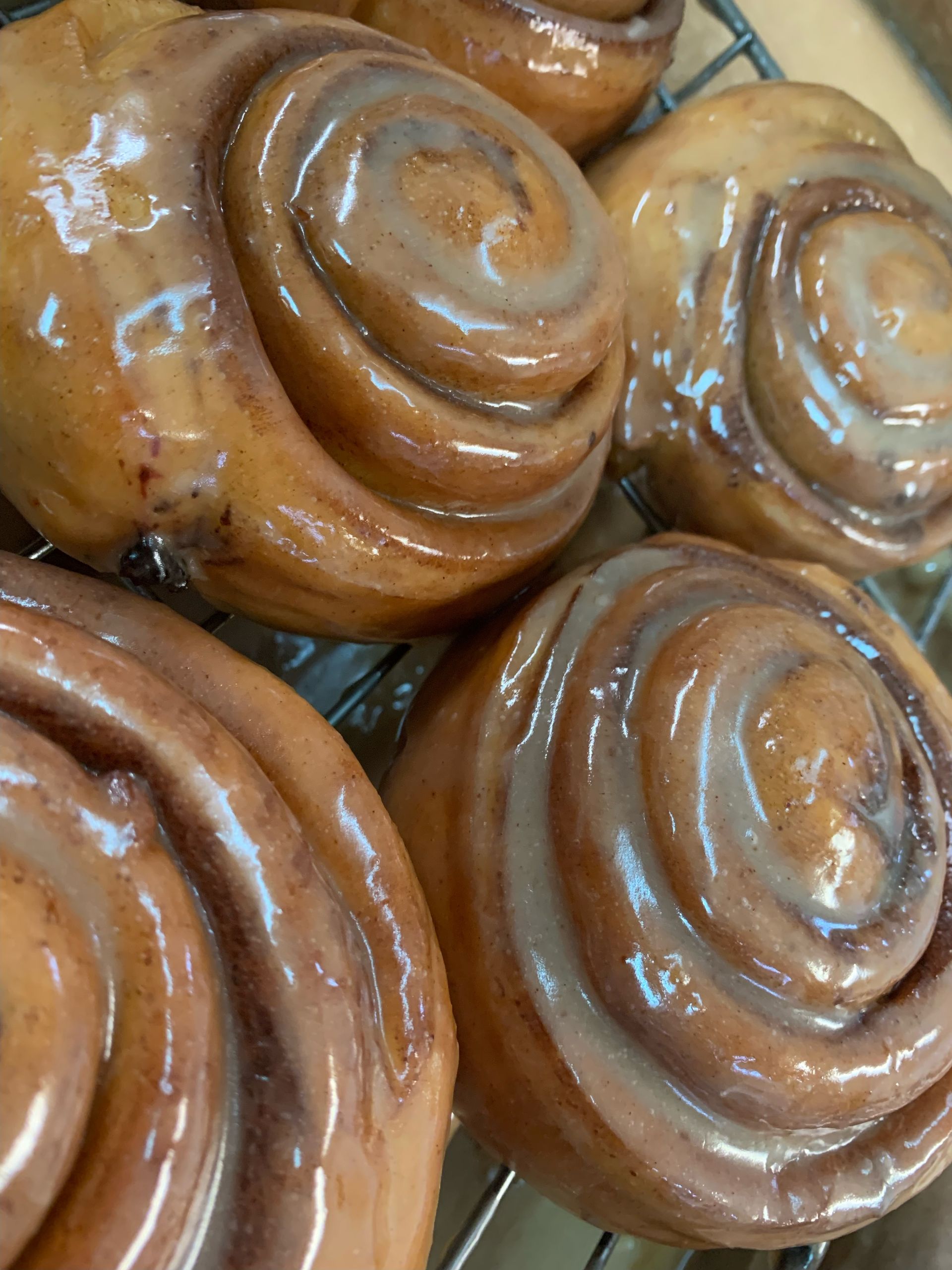 Close-up of glazed cinnamon rolls on a wire rack, brown, swirled, and glossy.