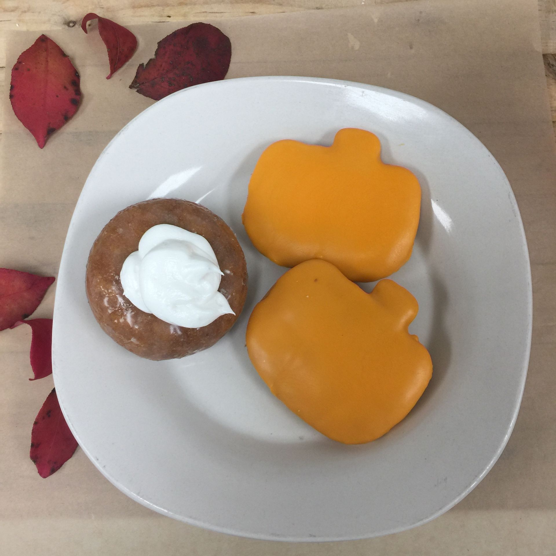 Plate with pumpkin-shaped cookies and a donut topped with whipped cream; red leaves nearby.