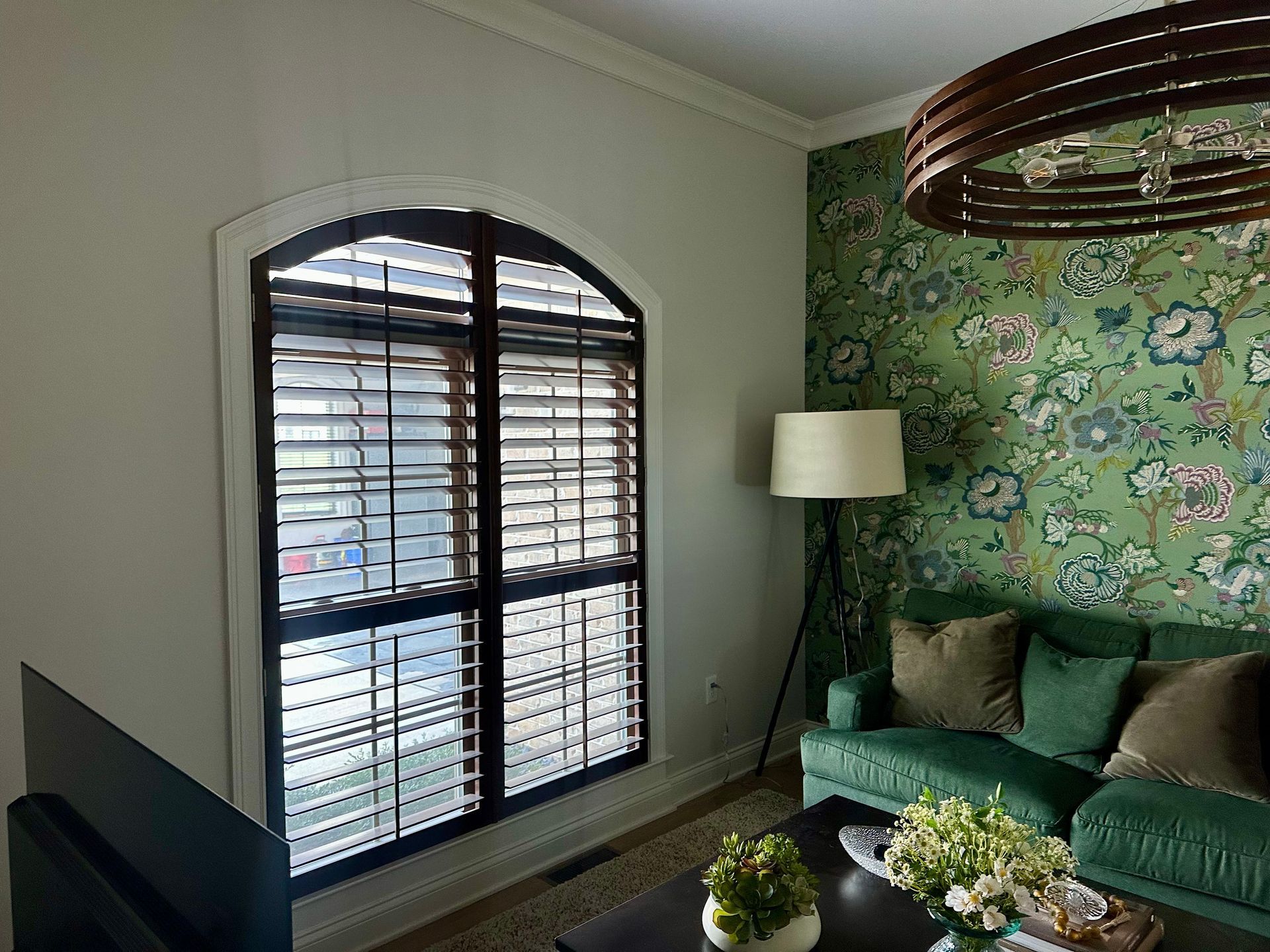 wood stain arch shutter panels, green floral wallpaper, green sofa, wood round chandelier