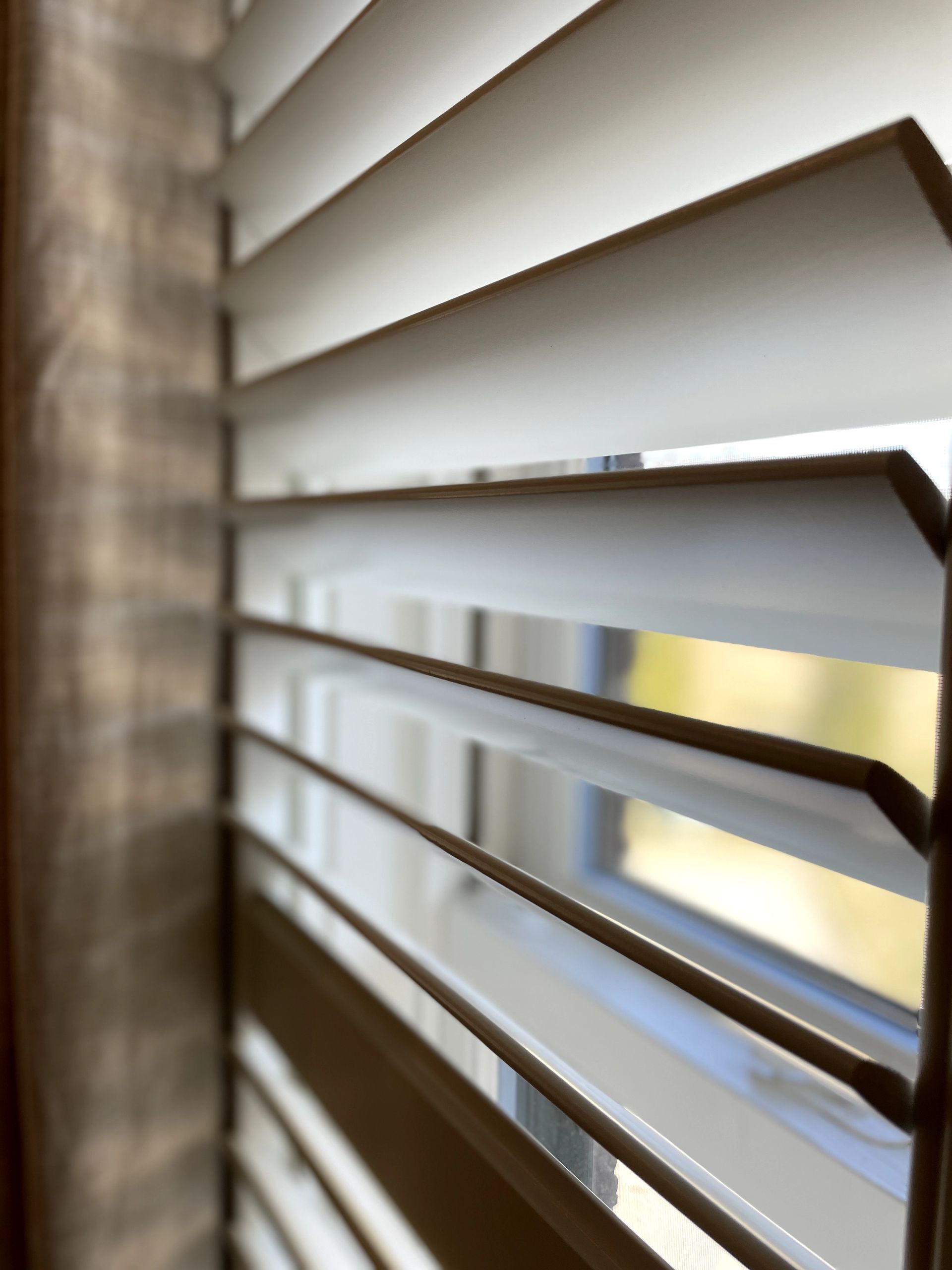 Close-up view of partially open, beige wooden blinds with light streaming through.
