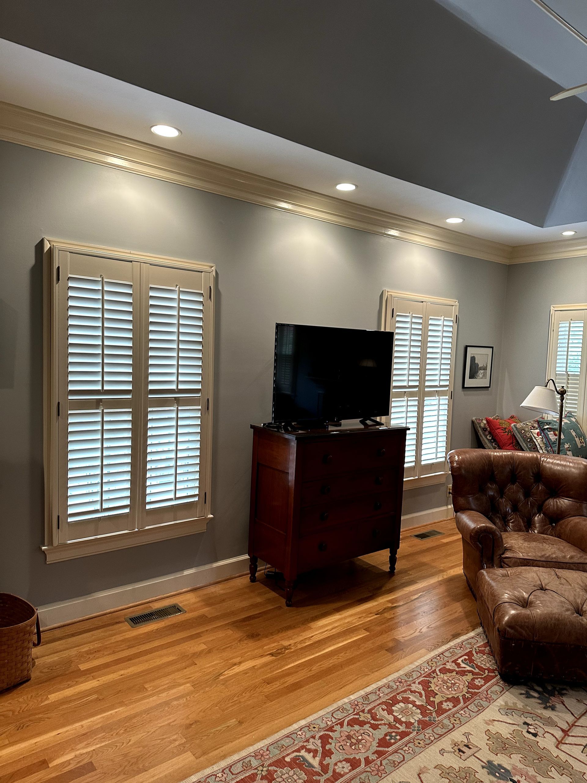 Living room with gray walls, wooden floor, shuttered windows, and a TV on a wooden cabinet.