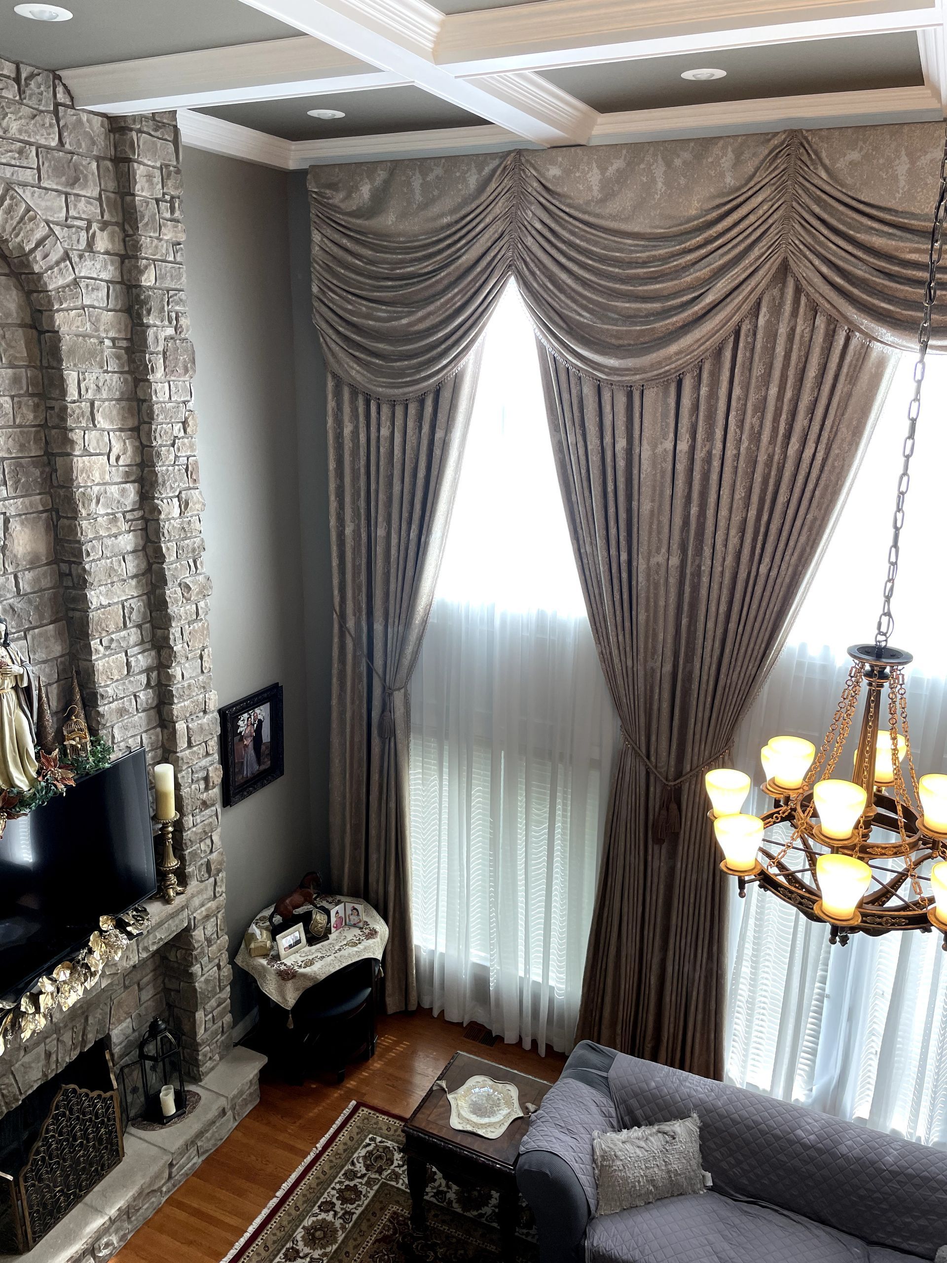High-ceiling living room with stone fireplace, ornate curtains, and a chandelier.