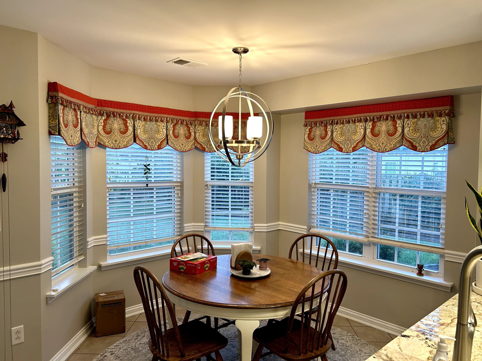 Bay window dining area with a round table, four chairs, and patterned valances.