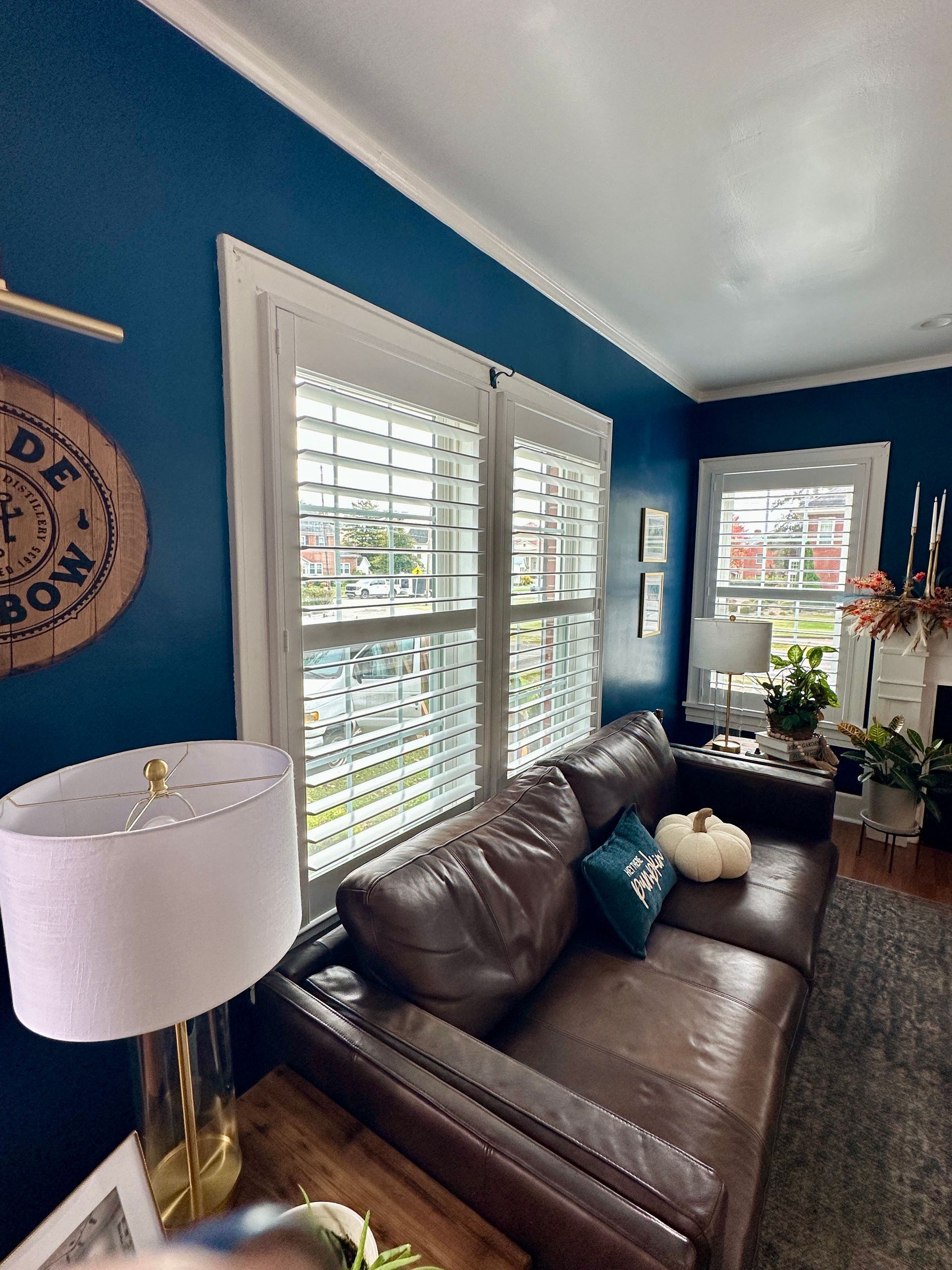 living room with white shutters, leather sofa, navy walls, fall decor