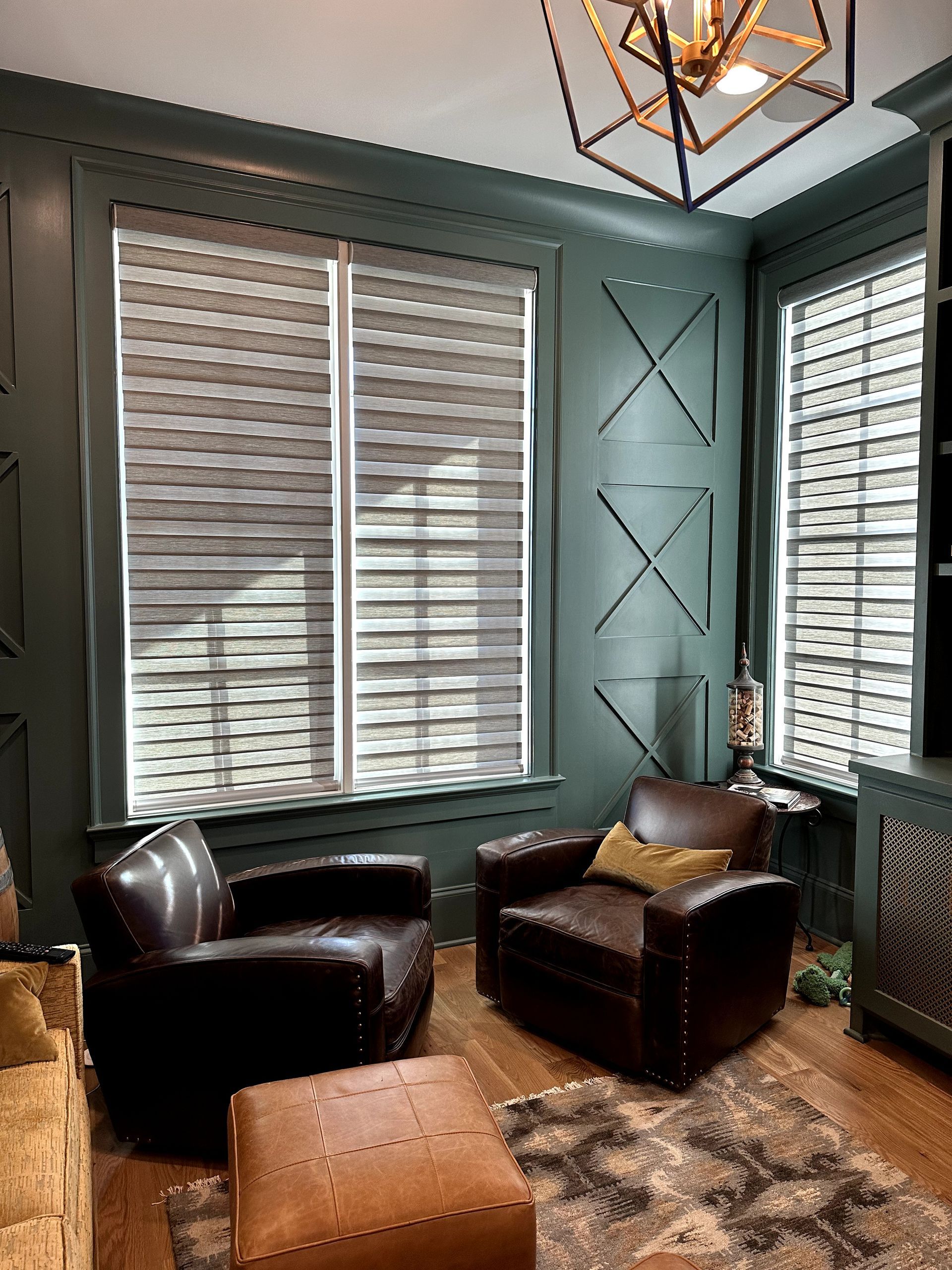 Cozy, dark green study with leather chairs and ottoman, patterned rug, and patterned window shades.