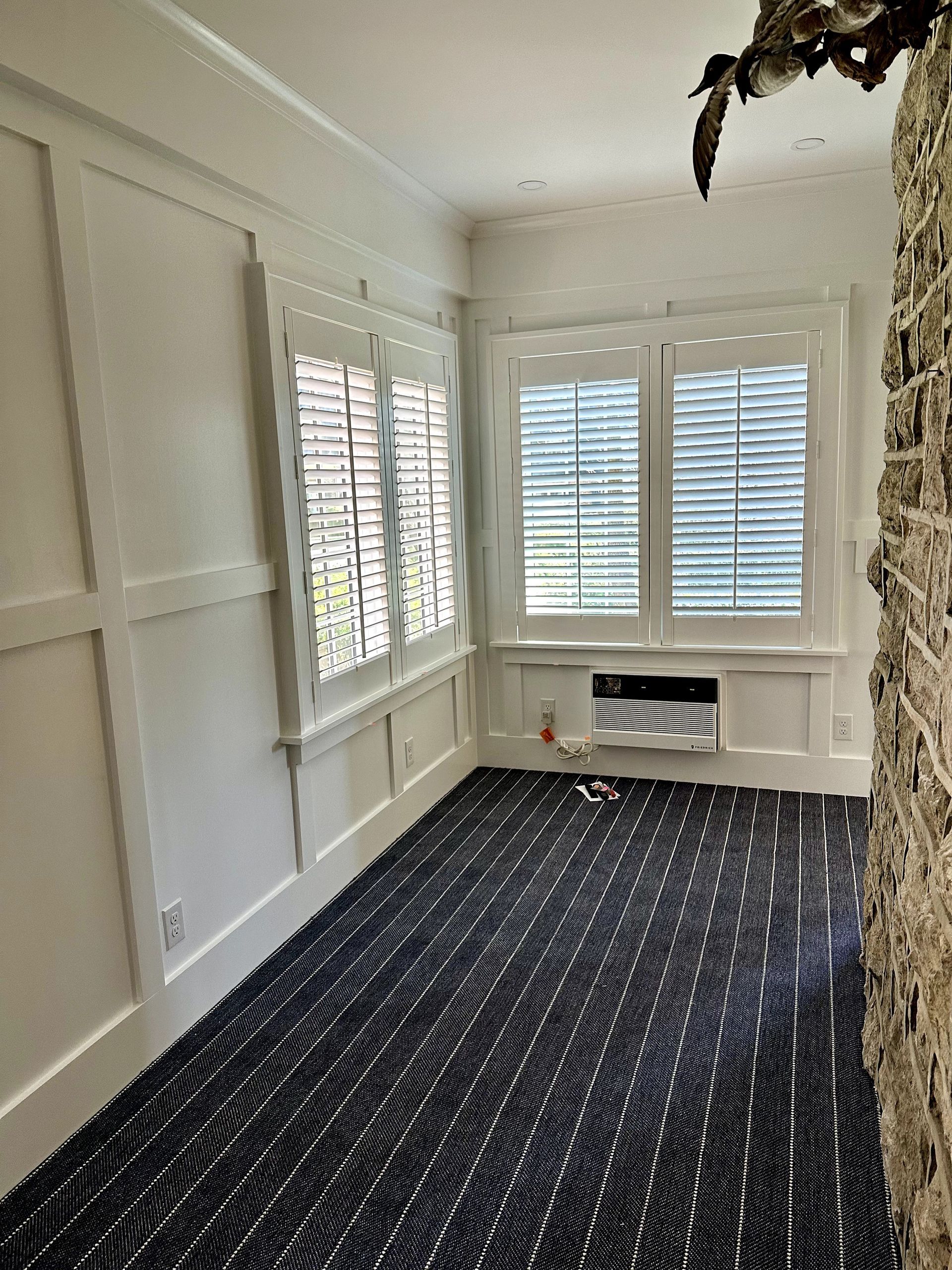 White-walled room with dark patterned carpet, shuttered windows, and ornate wall paneling.