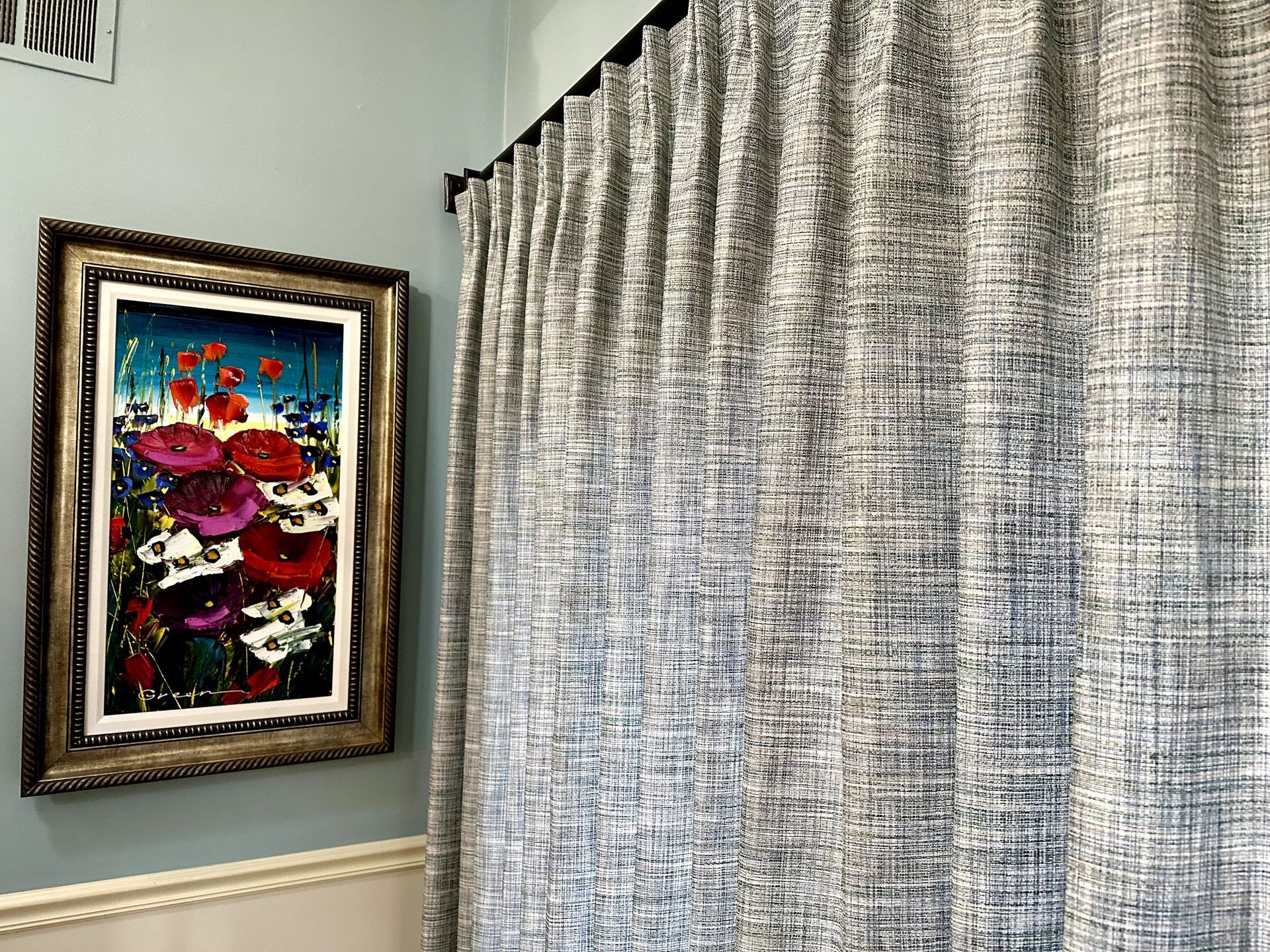 Colorful floral painting on a blue wall next to textured gray curtains.