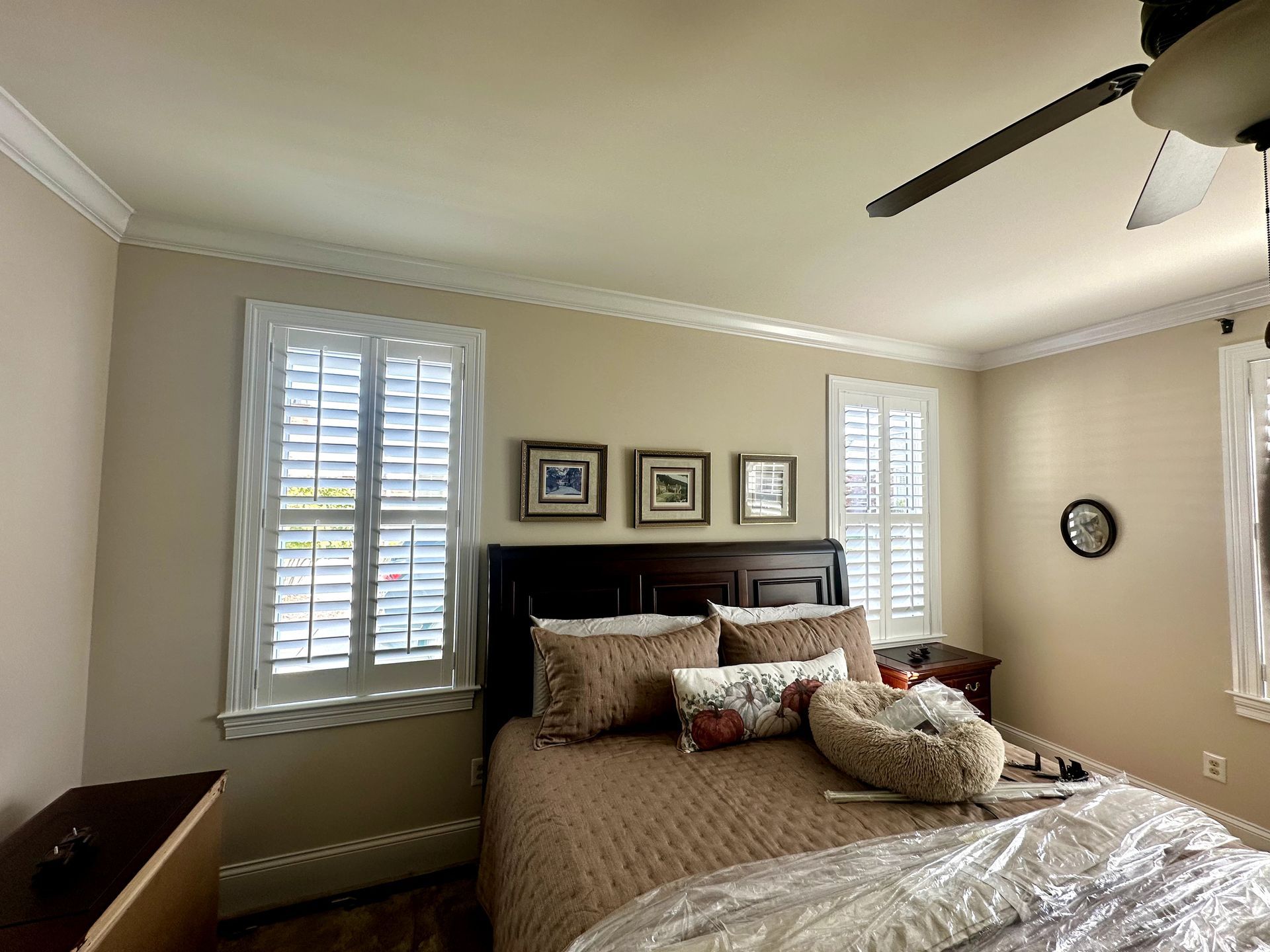 Bedroom with a bed, window shutters, beige walls, and decorative pillows.