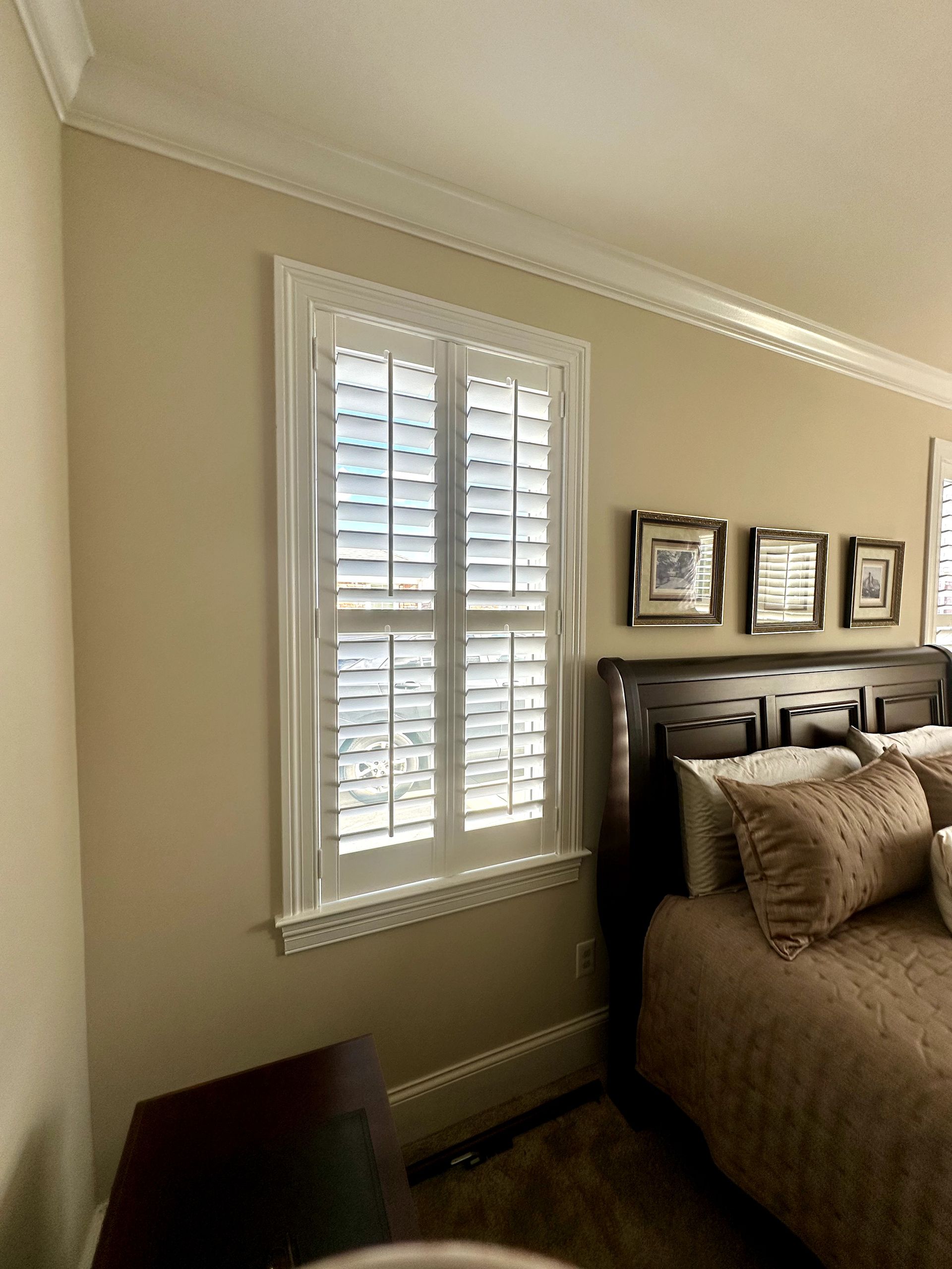 Bedroom with white shuttered window, tan walls, and a dark wood bed.
