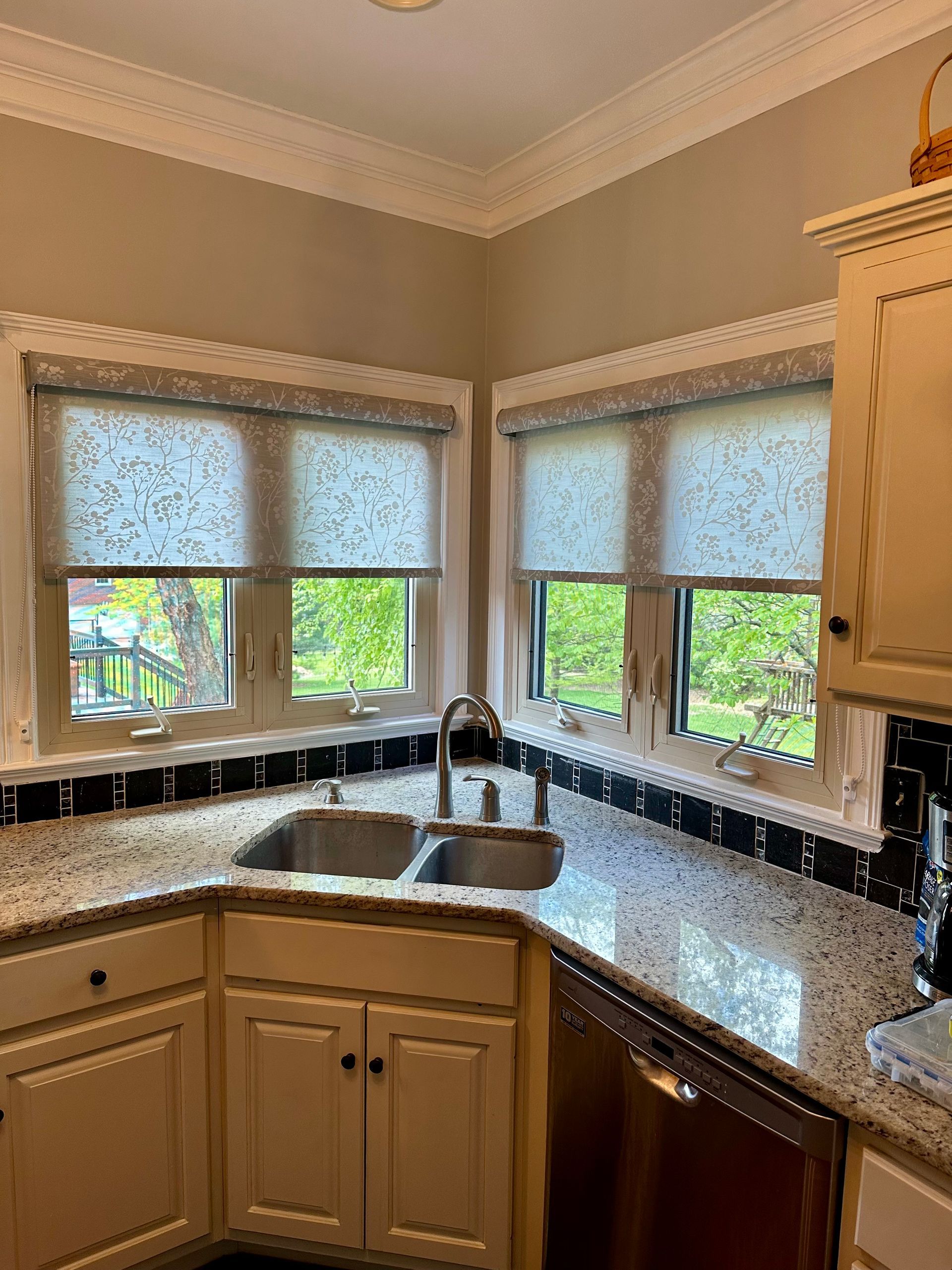 Kitchen corner with windows, a sink, granite countertops, and cream cabinets.