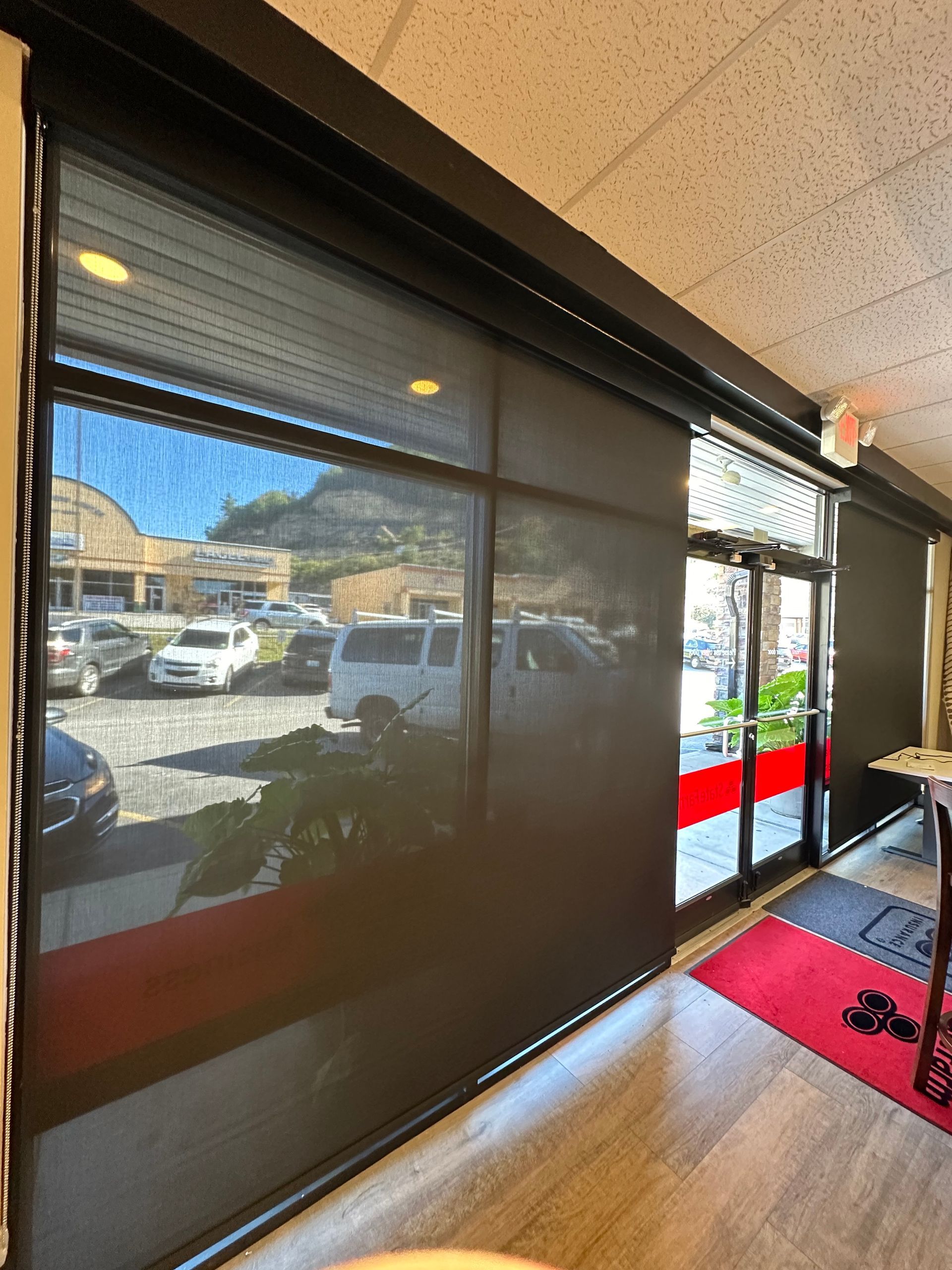 Black roller shades covering windows and a door, reflecting an outdoor scene of cars and buildings.