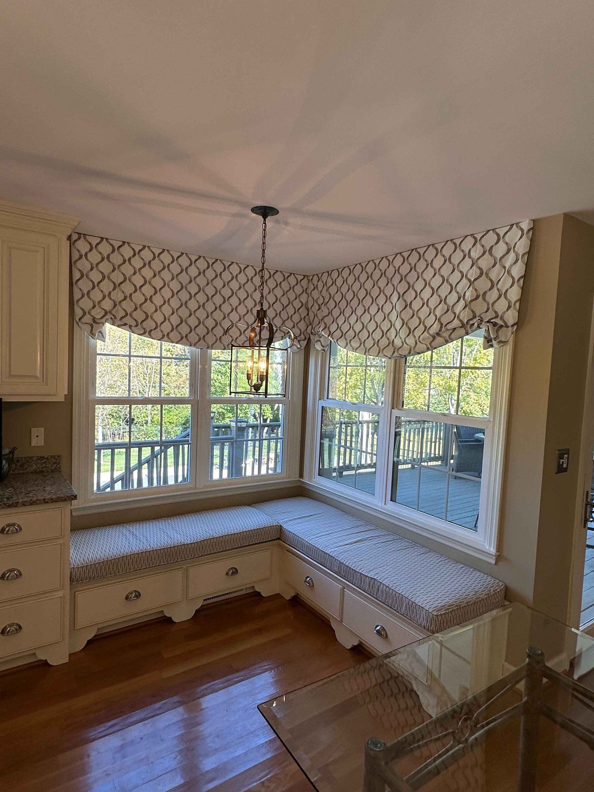 Bay window dining area with a round table, four chairs, and patterned valances.