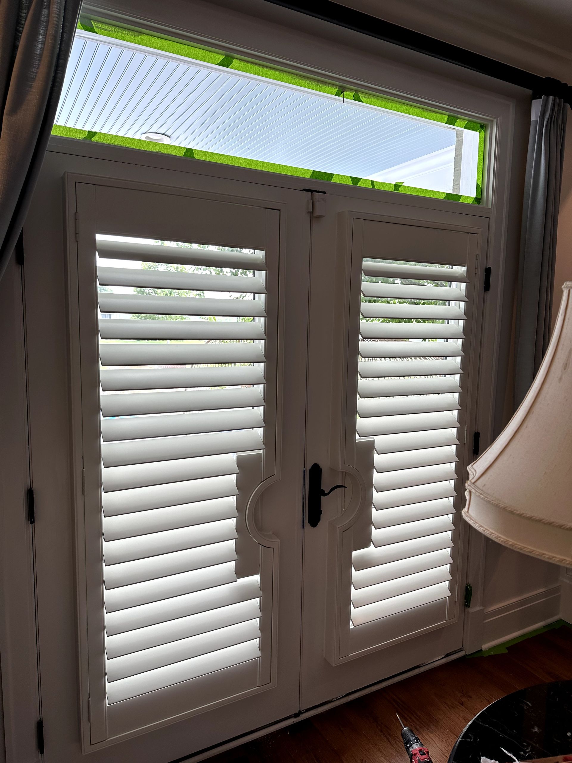 White shuttered French doors with a transom window, set in a room with a lamp.