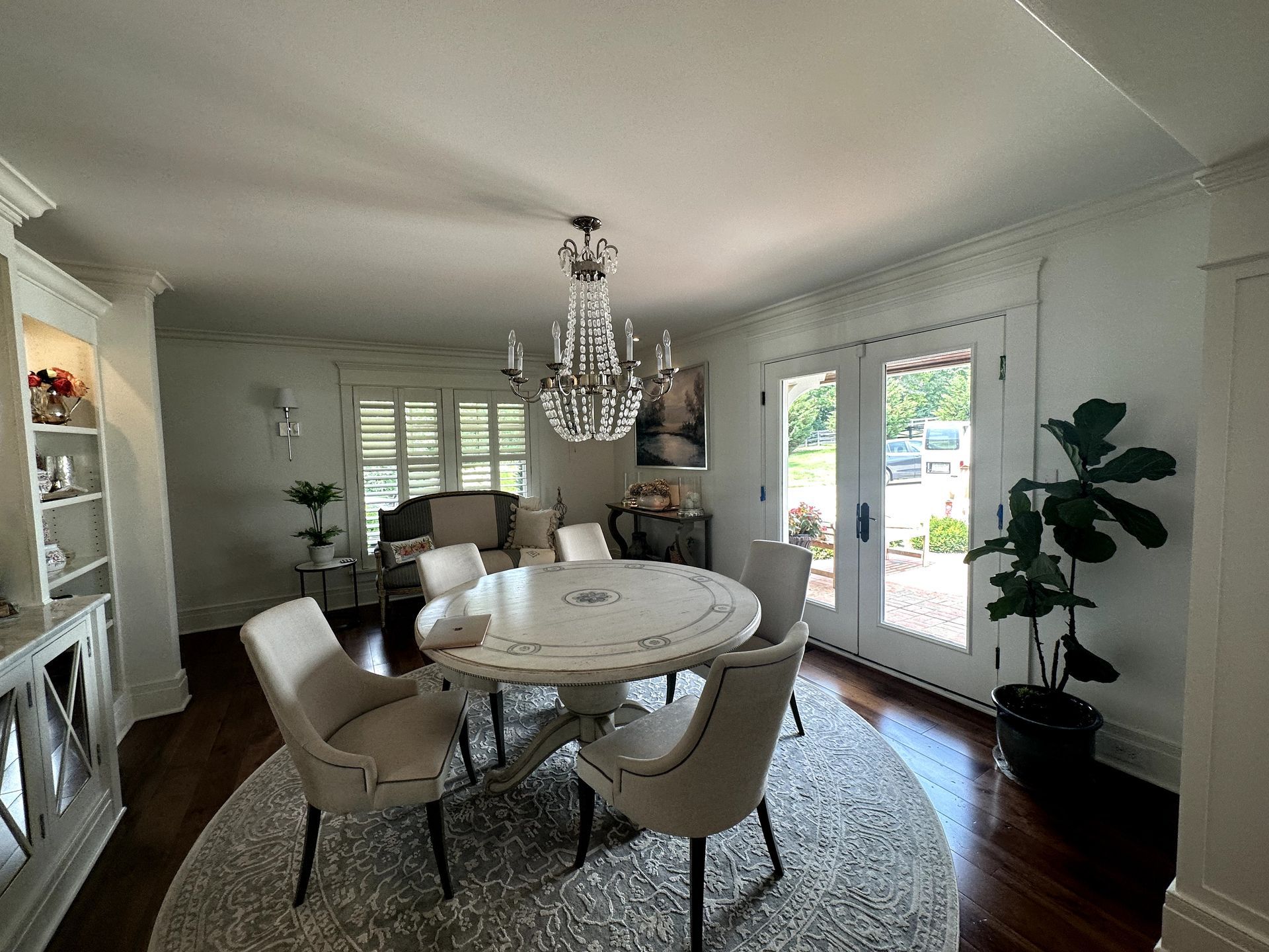Elegant dining room with round table, chandelier, and chairs on a rug. Doors and built-in shelves.